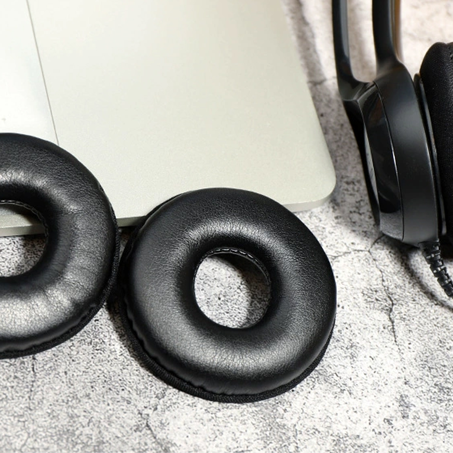 Zwei schwarze Ohrpolster und ein Headset vor hellgrauem Hintergrund, in der Nähe eines Laptops.