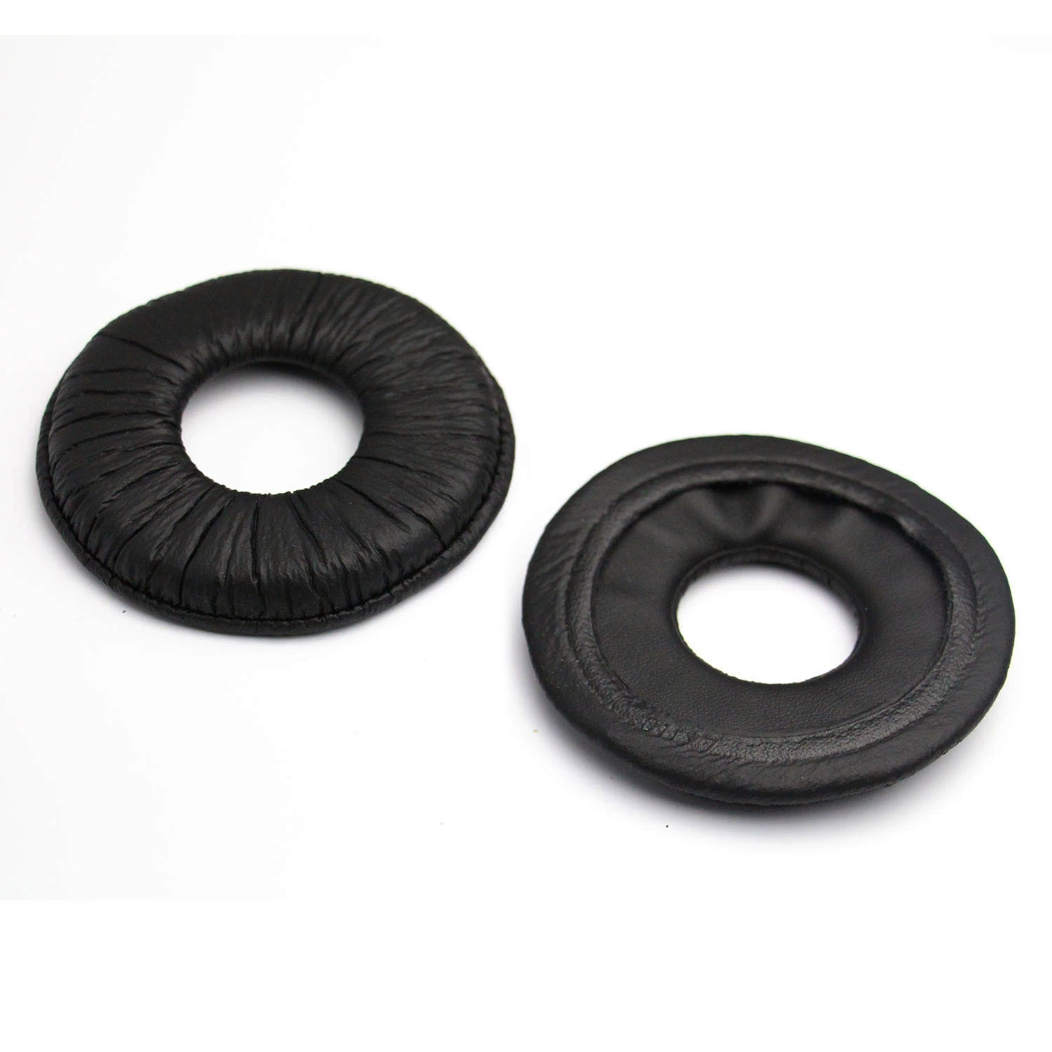 Dwie czarne, skórzane poduszki do słuchawek. Jedna jest cała, druga jest na lewą stronę.