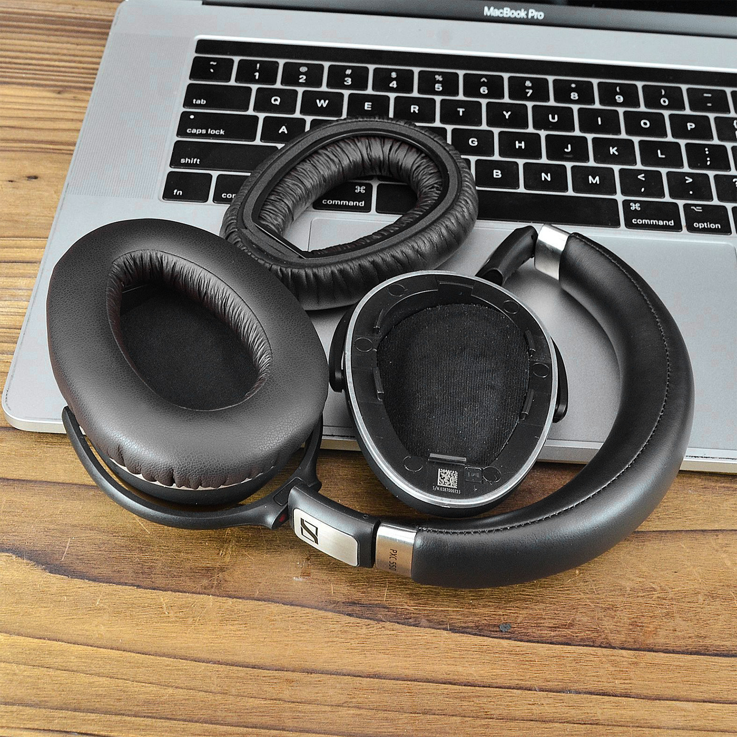 Laptop-Tastatur mit abgenommenen schwarzen Kopfhörern und Ohrpolstern auf Holz.