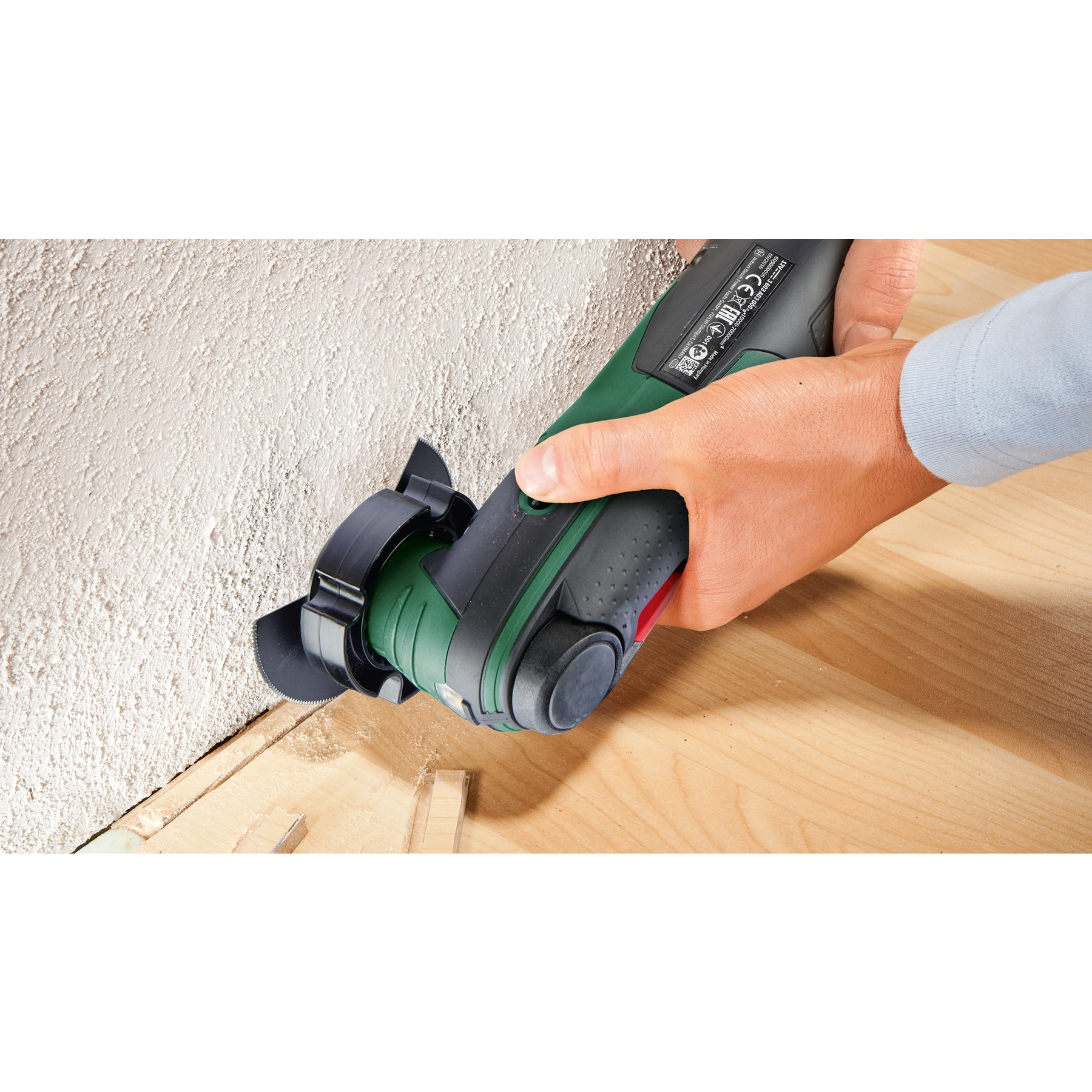 Hand hält grünes Elektrowerkzeug, schneidet Wand neben Holz.