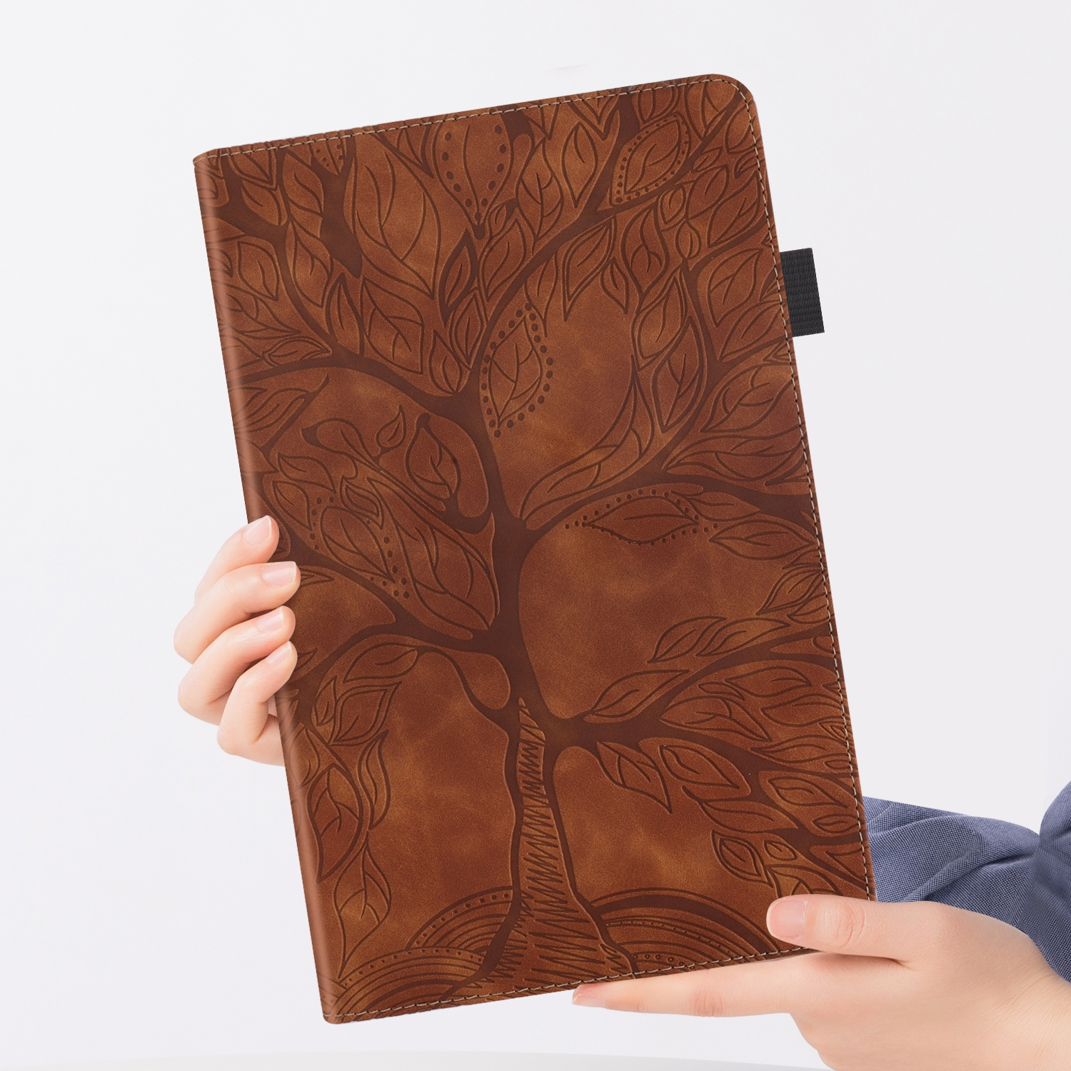 Person hält braune Leder-Tablethülle mit Baumdesign und schwarzem Riemen.