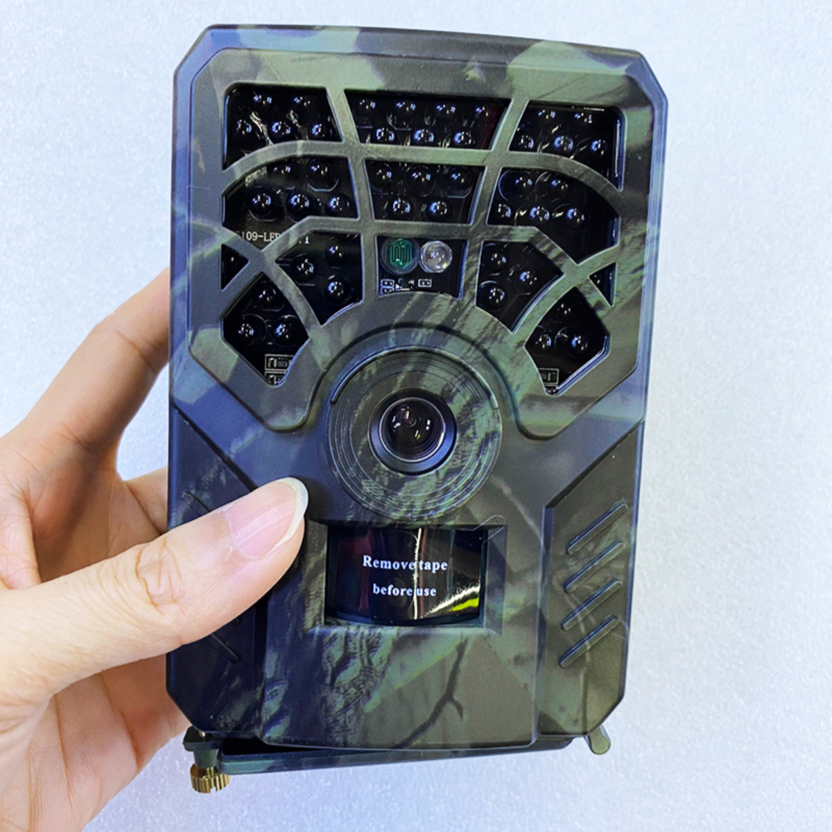 Eine Hand hält eine Tarn-Wildkamera. Die Kamera hat ein Objektiv und Infrarot-LEDs.