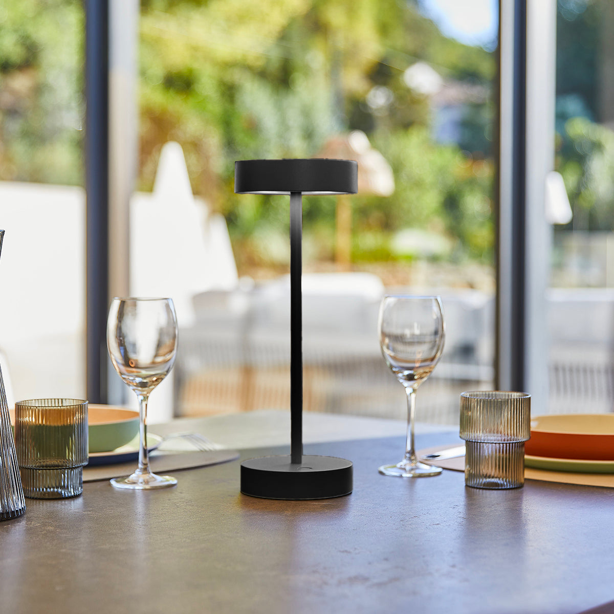 Schwarze moderne Lampe auf Tisch, Weingläser und Kerze. Hintergrund: Fenster, Außenansicht.