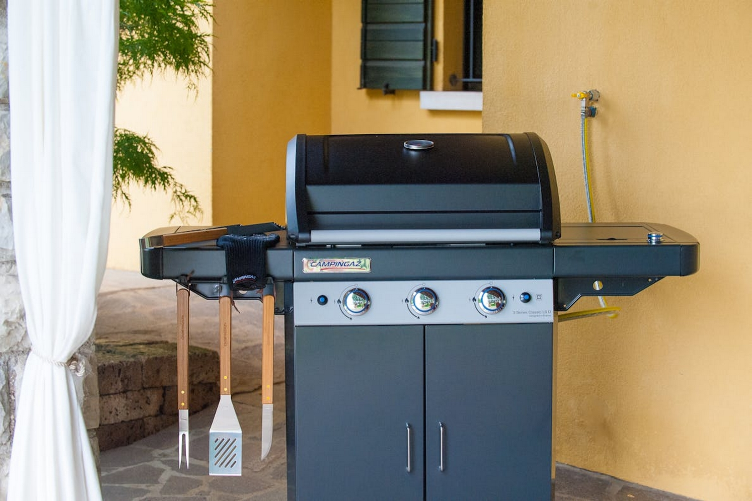 Griglia per barbecue all'aperto con attrezzi appesi al lato. La griglia è nera e grigia.