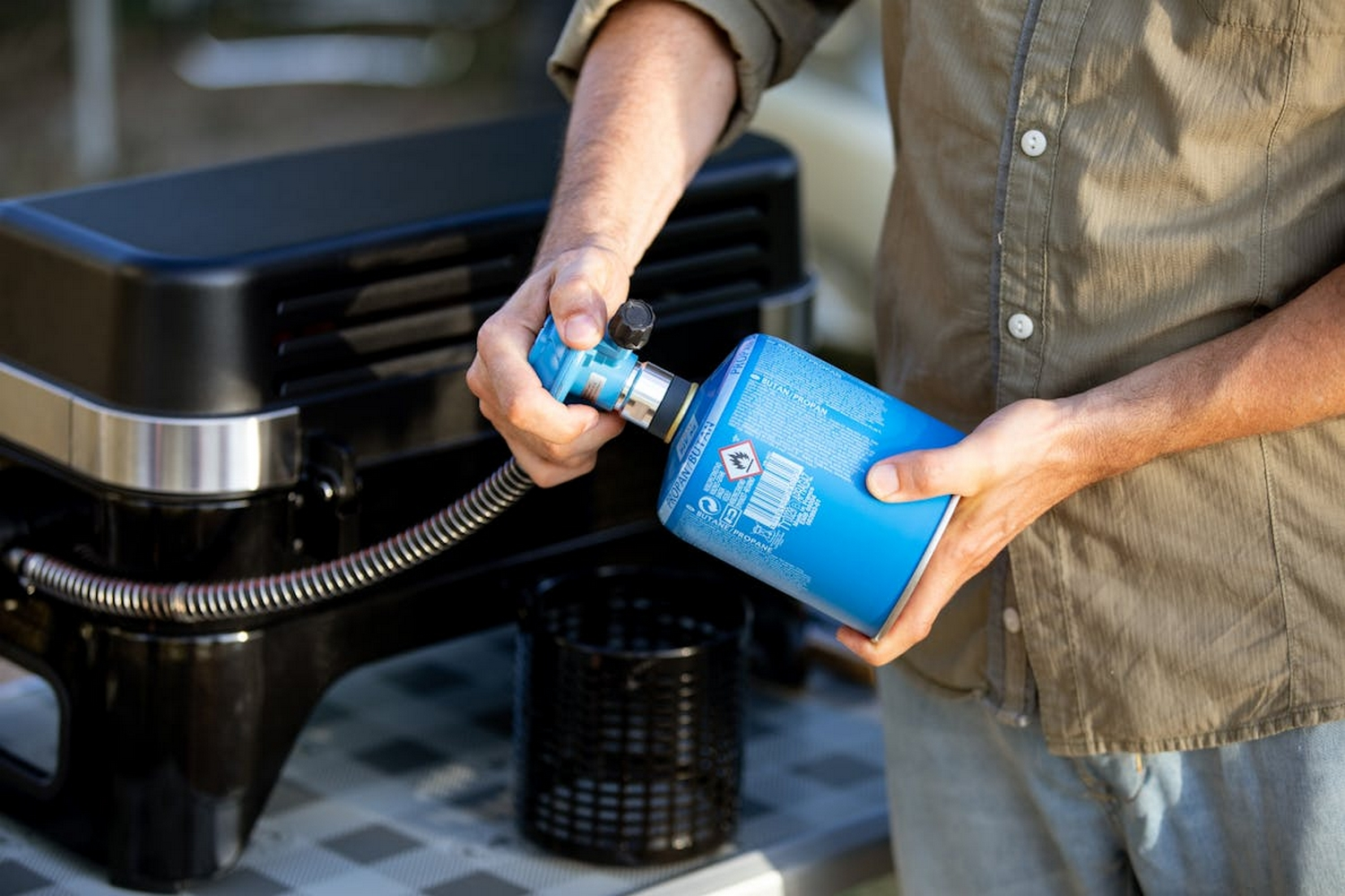 Een persoon die een blauwe gasfles aan een zwarte grill bevestigt, een barbecue voorbereidend.