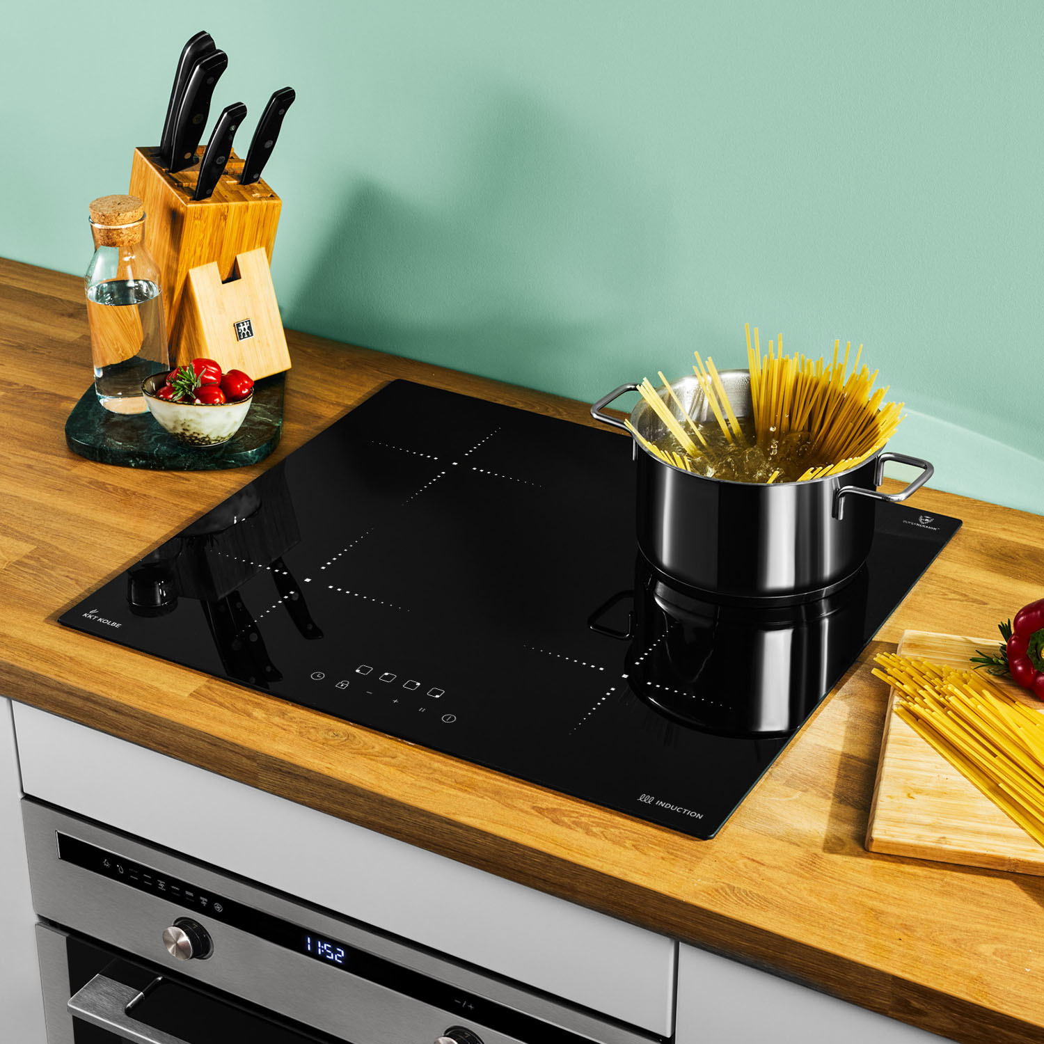 Schwarzes Induktionskochfeld mit einem Topf mit kochendem Wasser und Spaghetti. Holz-Arbeitsplatte, türkisfarbener Hintergrund.