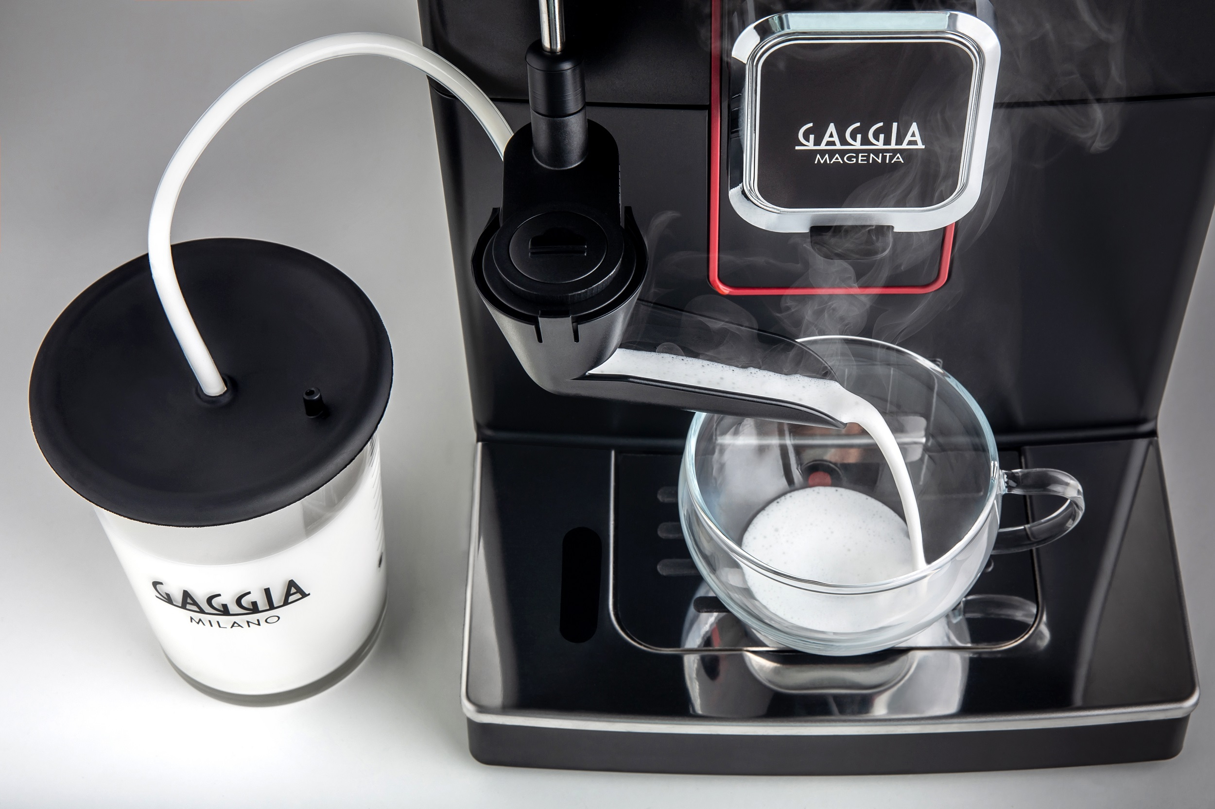 Kaffeemaschine gießt Milch in eine Glastasse. Weißer Behälter links.