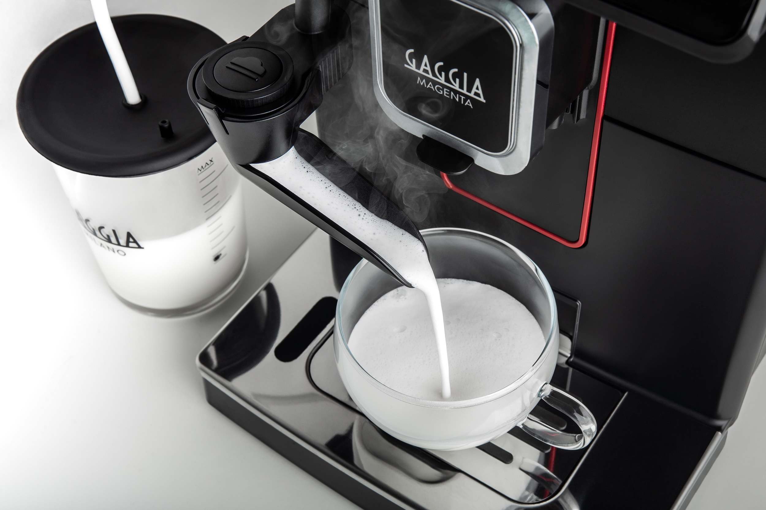 Espressomaschine gießt Milchschaum in eine Glastasse. Ein Milchbehälter ist links sichtbar.