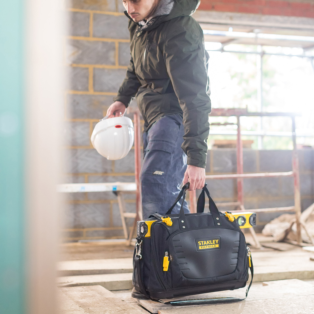 Bauarbeiter hält Helm und Werkzeugtasche auf einer Baustelle.