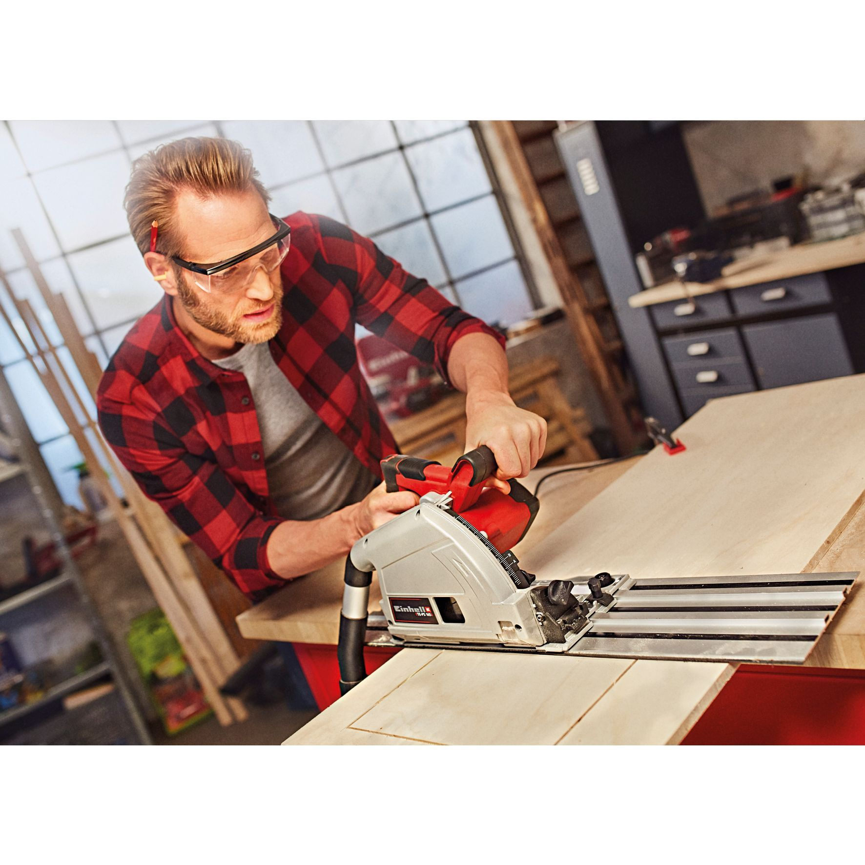 Mężczyzna w koszuli w kratę tnie drewno piłą tarczową w warsztacie.
