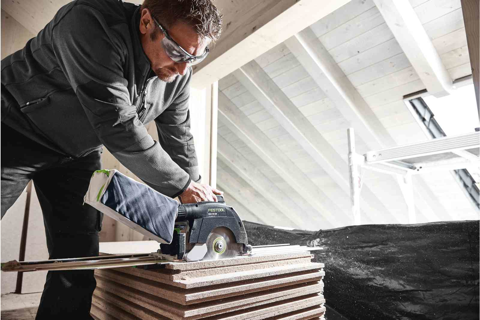 Mężczyzna używający piły tarczowej do cięcia stosu drewnianych desek na budowie.