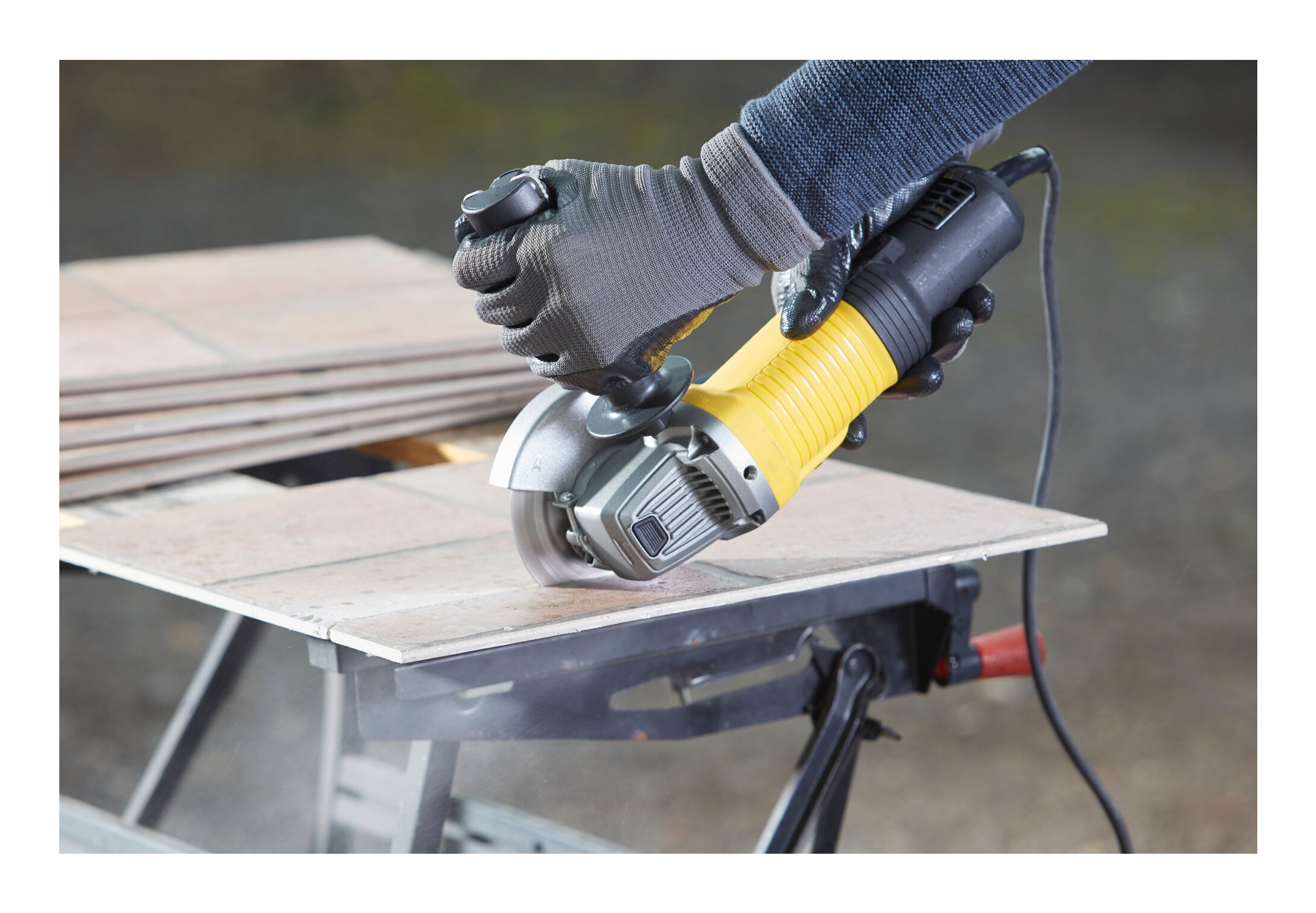 Osoba tnie płytkę szlifierką kątową. Szlifierka jest żółta i czarna.