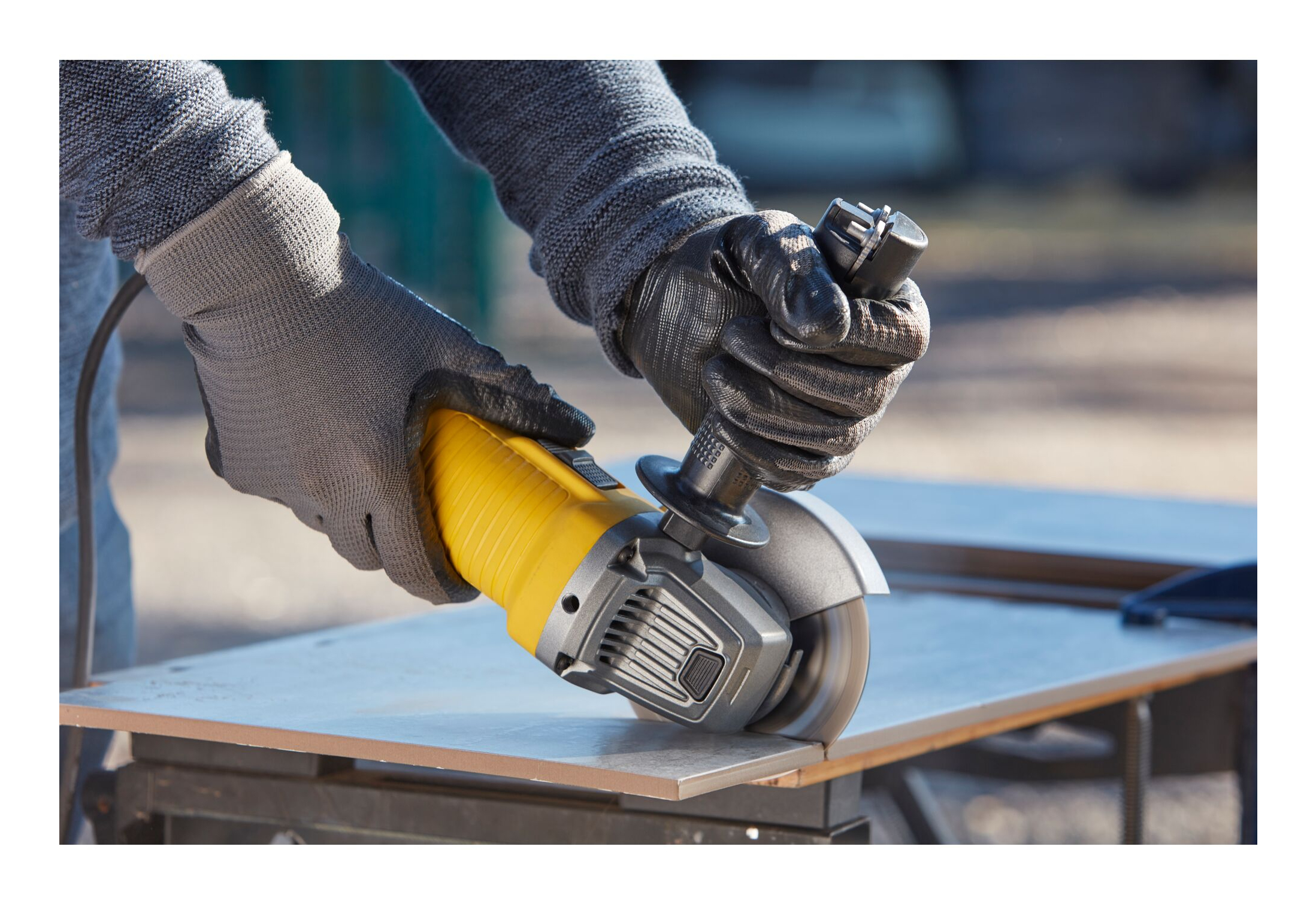 Dłonie w rękawicach używają żółtej szlifierki kątowej na płytce.