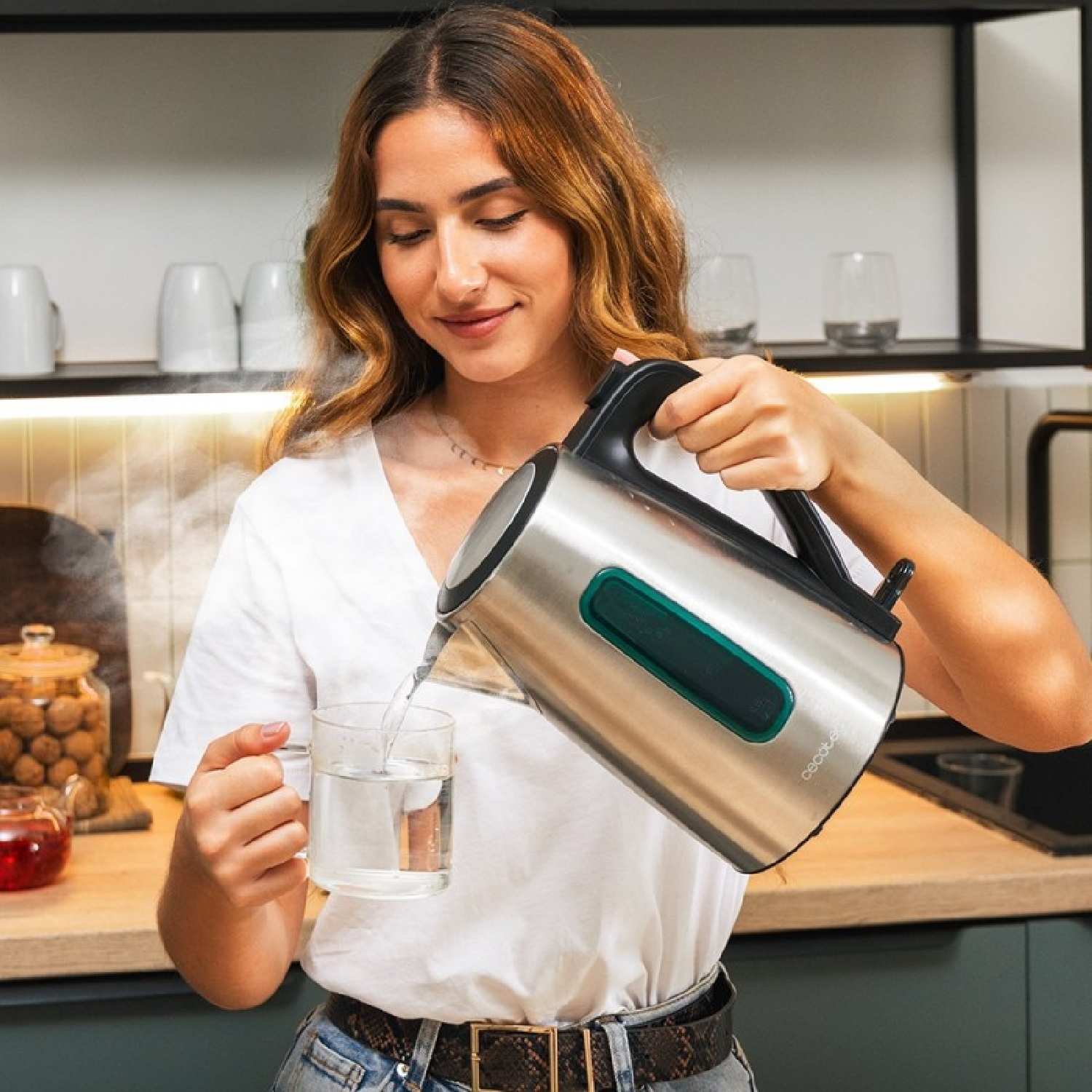 Vrouw die water uit een zilveren ketel in een glas giet.