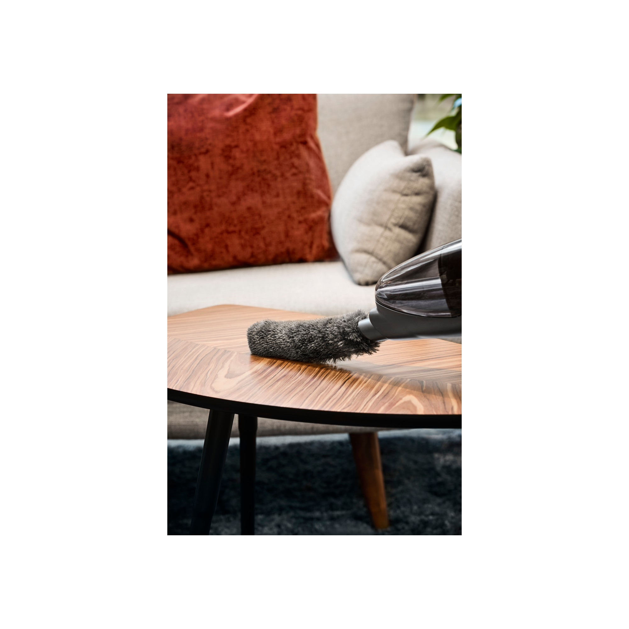 Końcówka odkurzacza czyszcząca drewniany stół, z kanapą w tle.