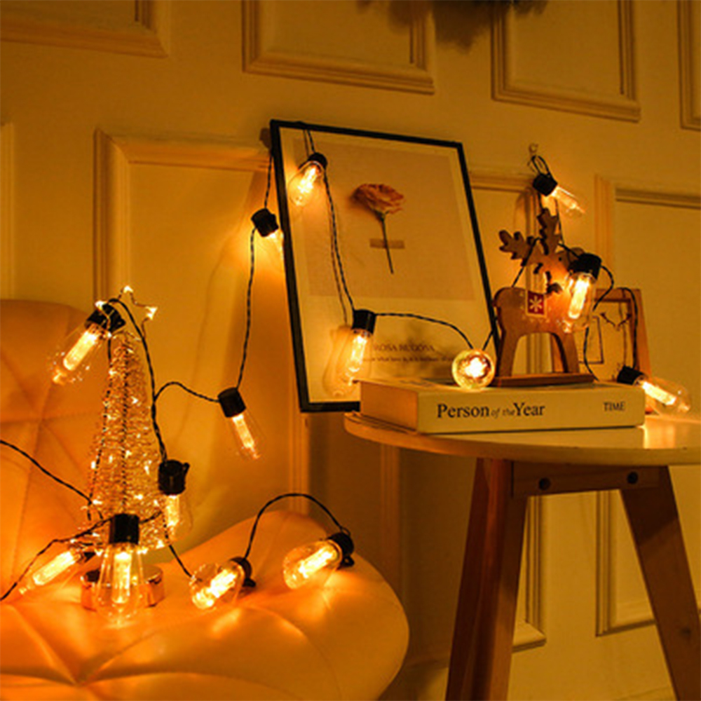 Weihnachtsbeleuchtung mit Rentier-Ornament und einem gerahmten Bild auf einem Tisch. Die Wand ist gelb.