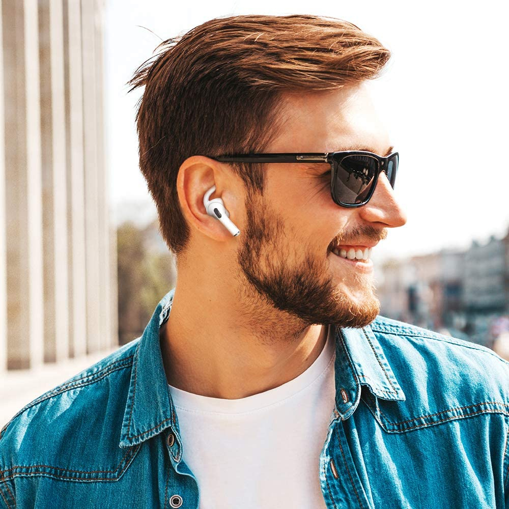 Ein Mann mit Sonnenbrille und Ohrhörern lächelt. Er trägt eine Jeansjacke.