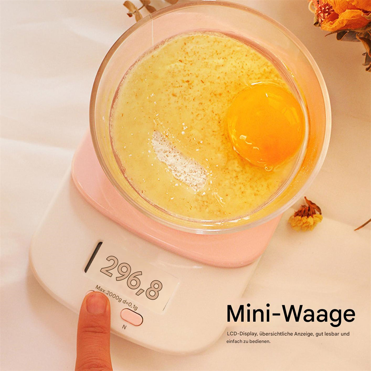 Eigelb in einer Schüssel auf einer rosa Waage. Ein Finger berührt die Ein/Aus-Taste. Getrocknete Blumen im Hintergrund.
