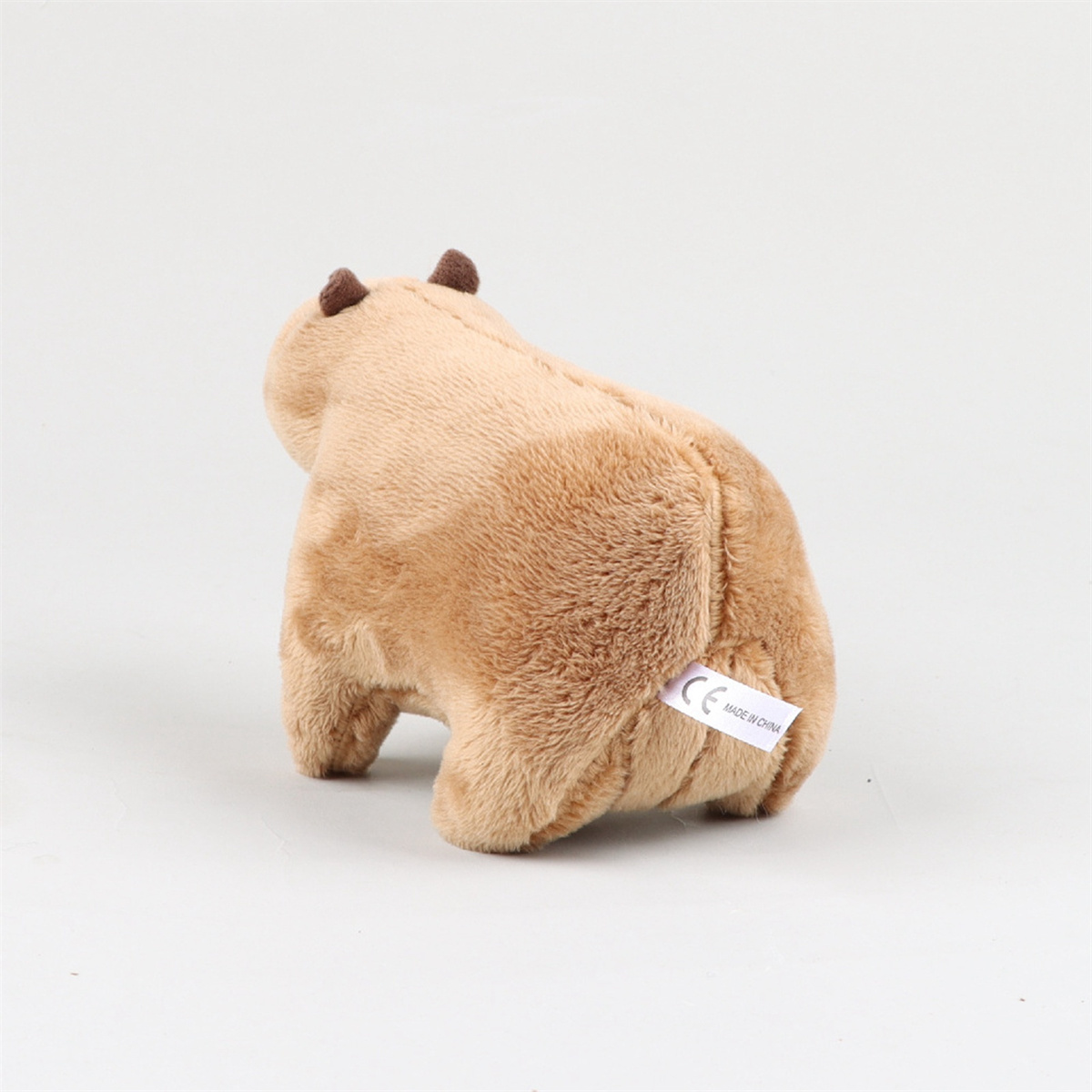 Hellbraunes Stofftier Capybara von hinten gesehen, auf weißer Oberfläche.