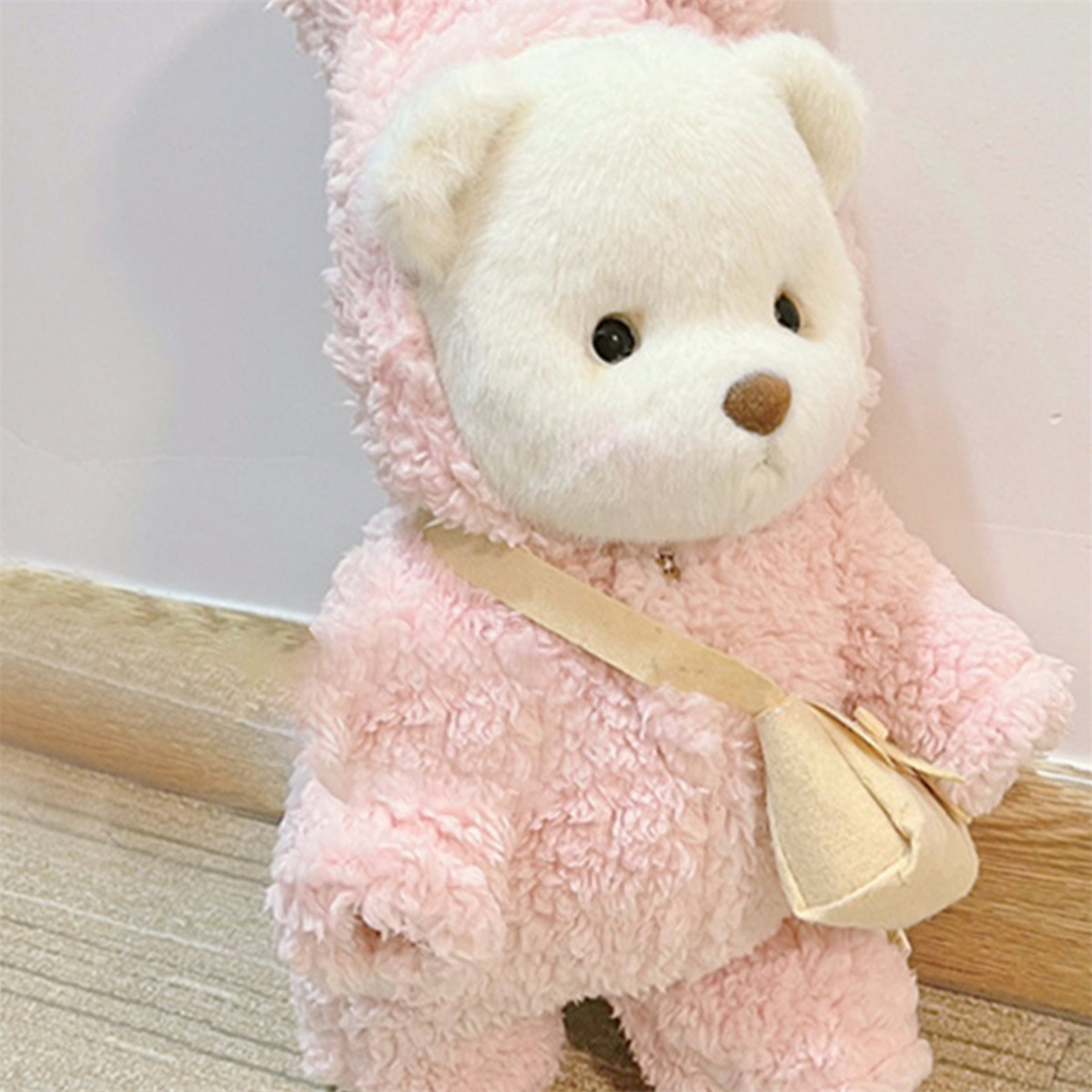 Ein rosa Teddybär in einem rosa Outfit mit einer kleinen Tasche, der in die Kamera schaut.