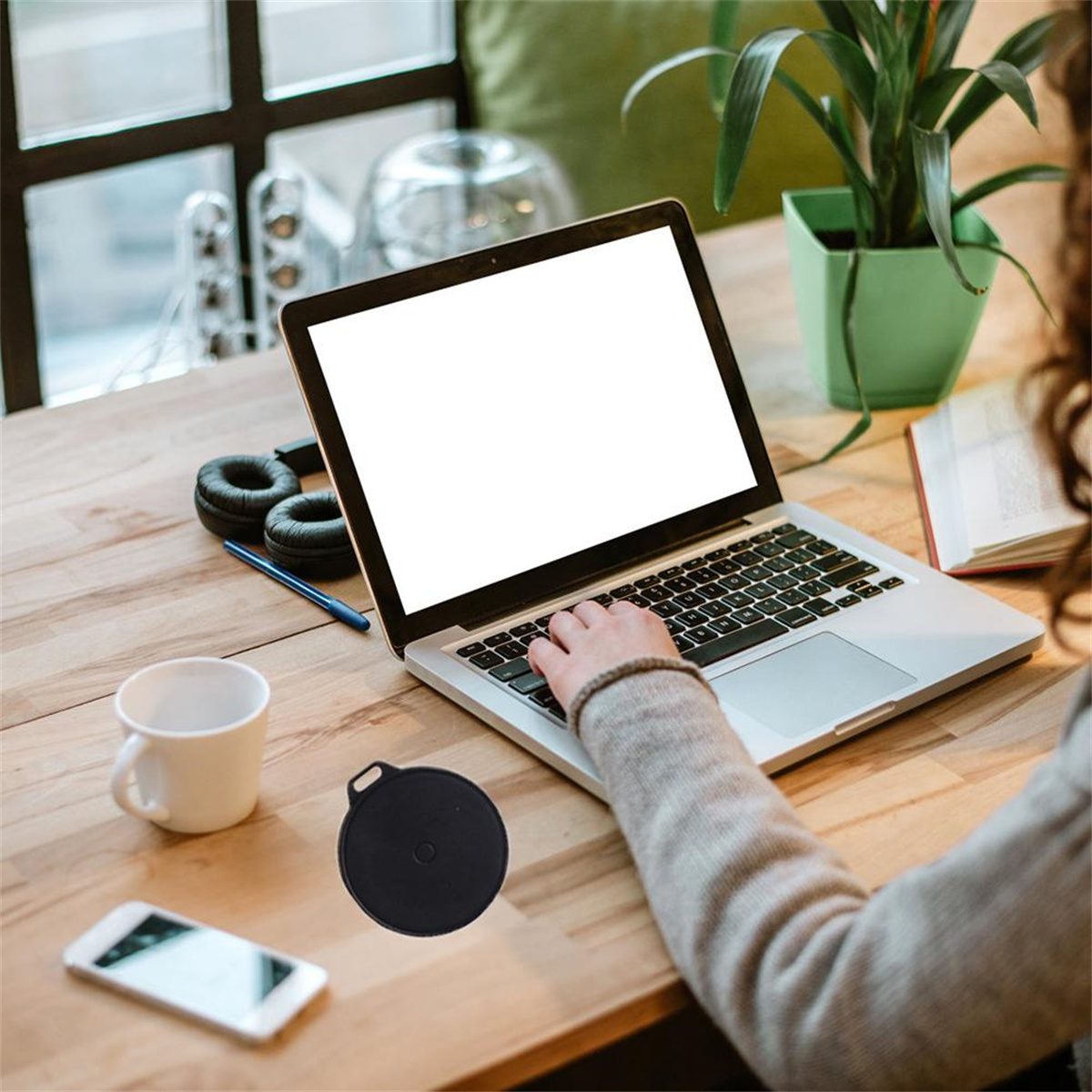 Person arbeitet an Laptop mit Telefon, Tasse und Kopfhörern auf Holztisch.
