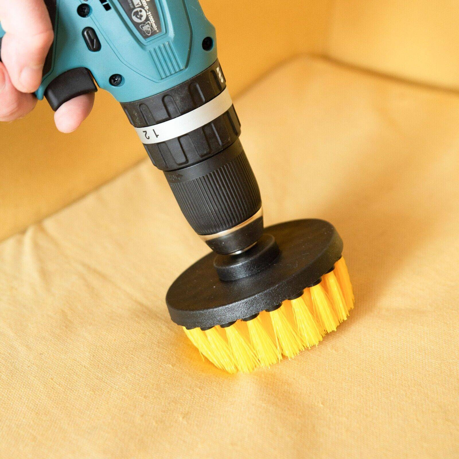 Eine Bohrmaschine mit gelb-schwarzem Bürstenaufsatz reinigt eine gelbe Couch. Nahaufnahme.