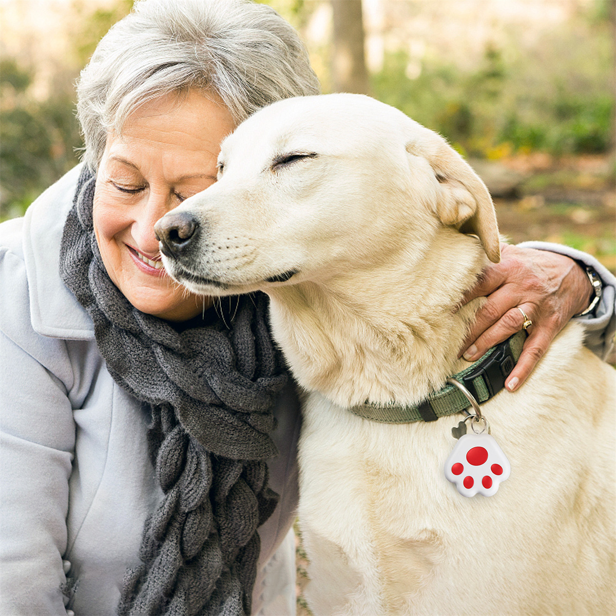 Eine Frau umarmt einen beigen Hund mit Pfotenanhänger, draußen, lächelnd.