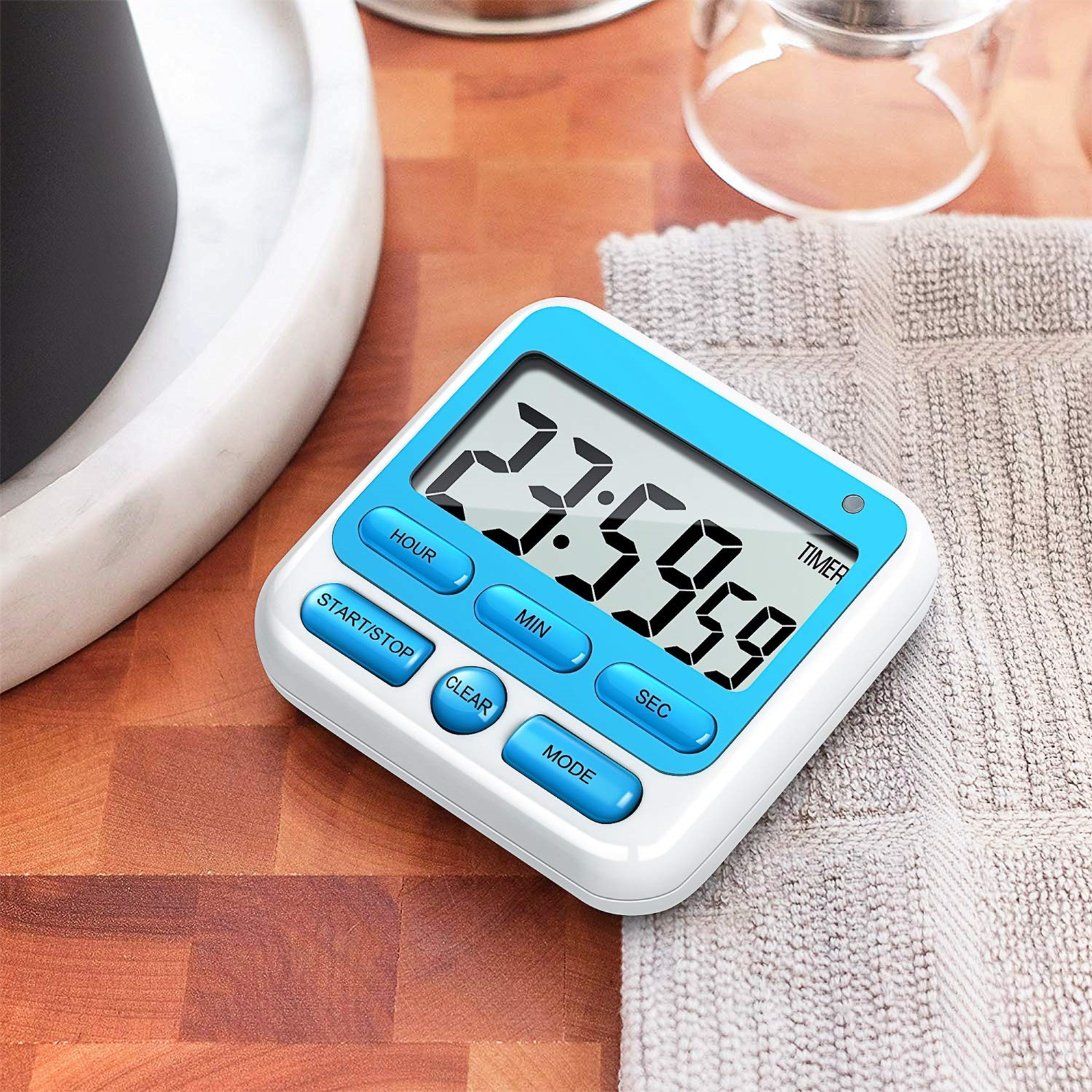 Ein weiß-blauer digitaler Timer mit Knöpfen. Die Anzeige zeigt 23:59:59. Ein Handtuch liegt daneben.