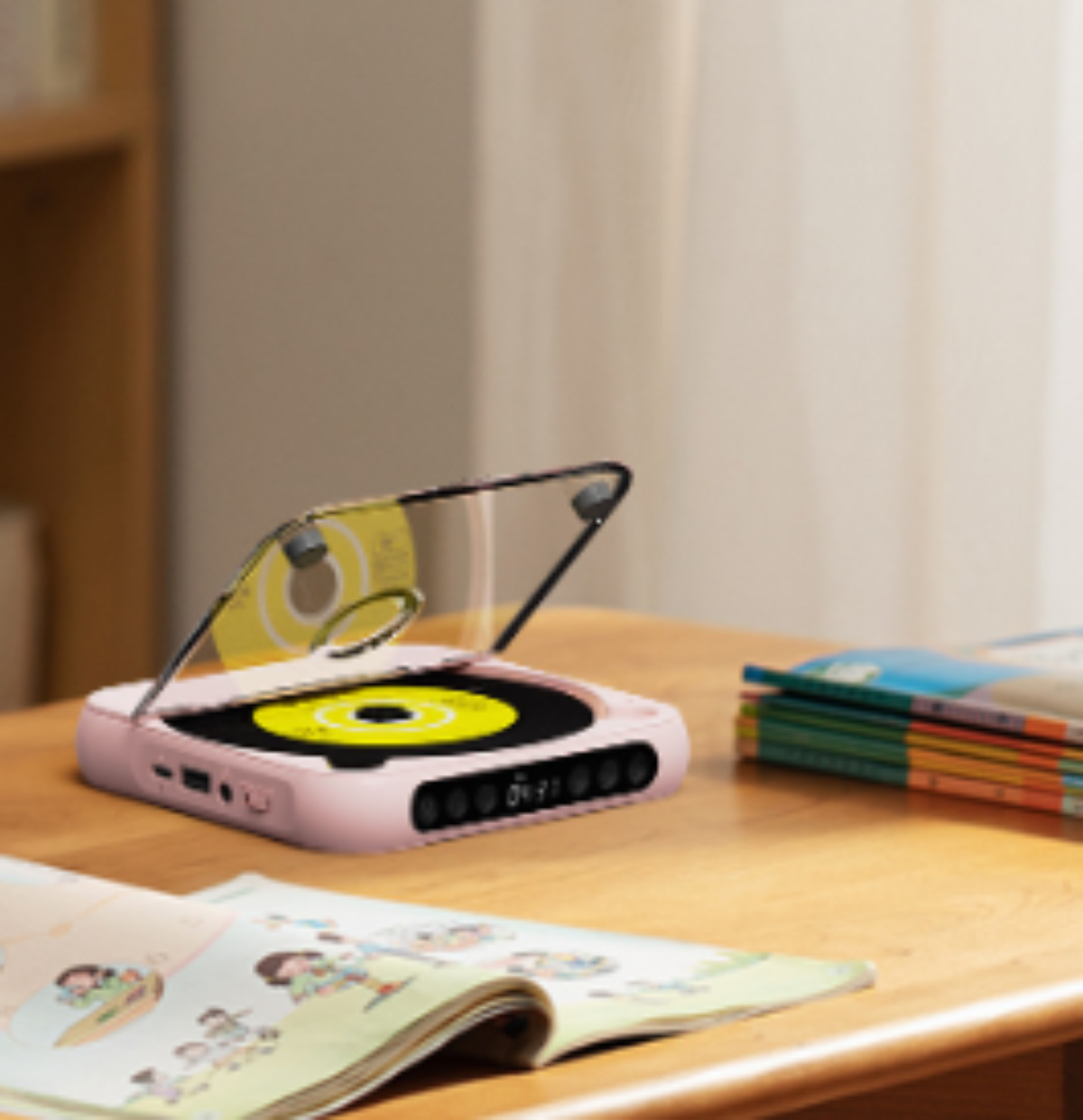 Ein rosa CD-Player im Retro-Stil steht auf einem Holztisch mit einem Buch, Innenaufnahme.