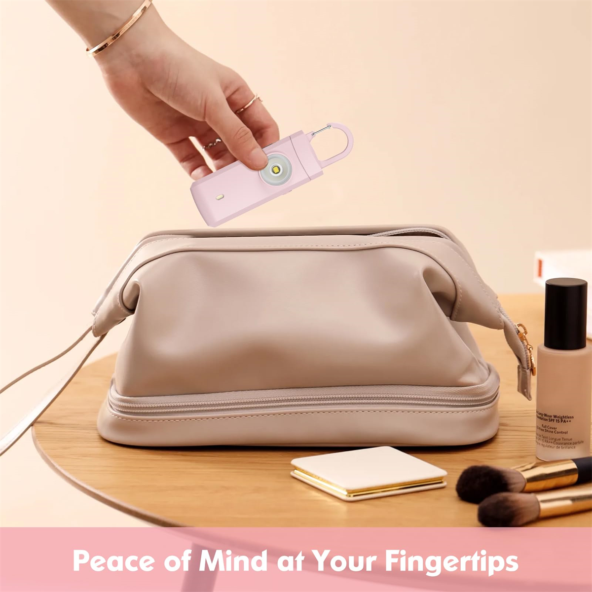 Hand hält einen rosa Personenalarm über einer Make-up-Tasche auf einem Tisch, Kosmetikartikel daneben.