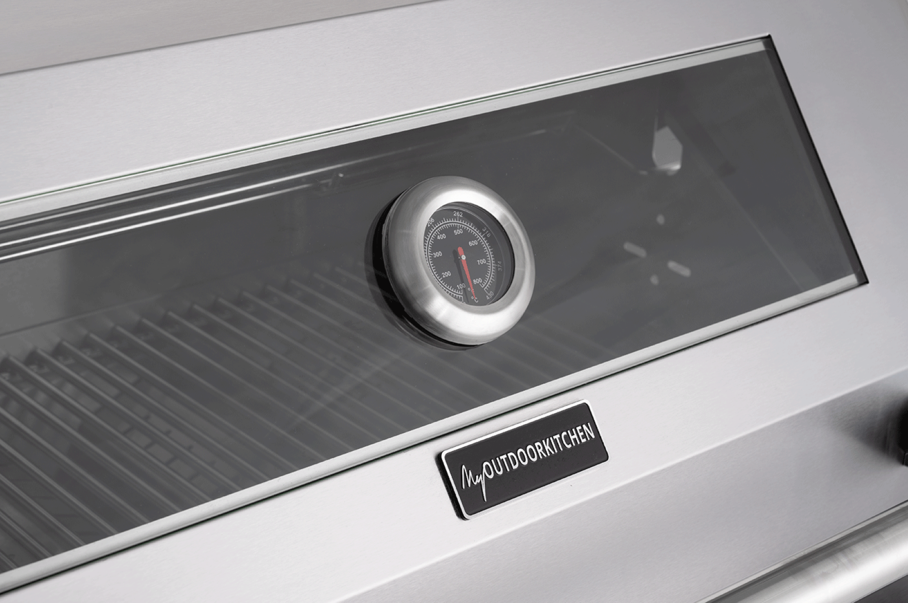 Grill aus Edelstahl. Thermometer und My Outdoor Kitchen-Etikett sichtbar. Schwarzer Hintergrund.