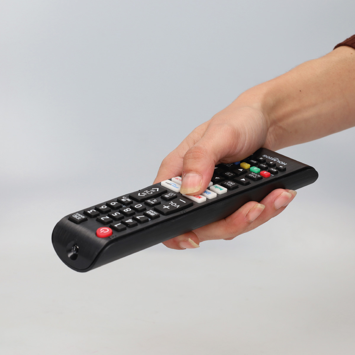 Persona sosteniendo un mando a distancia de TV negro con botones.