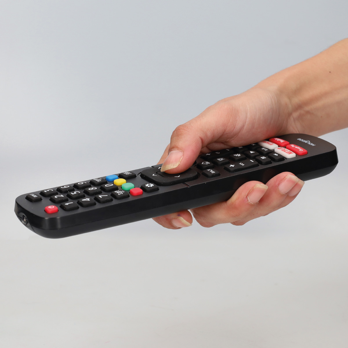 Mano sosteniendo un control remoto negro con botones coloridos sobre fondo gris.