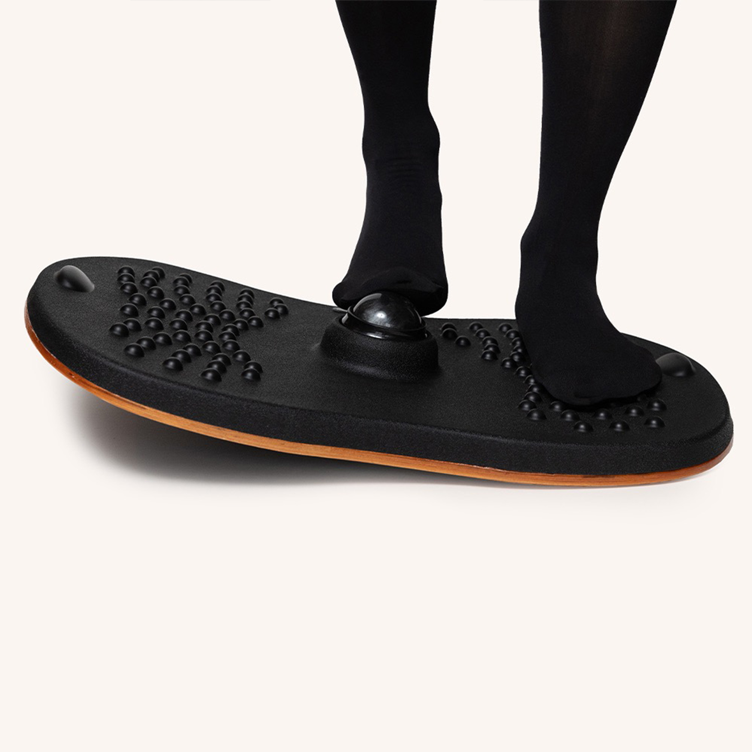 Die Beine und Füße einer Person auf einem schwarzen Balance Board mit Massagenoten, auf hellem Hintergrund.