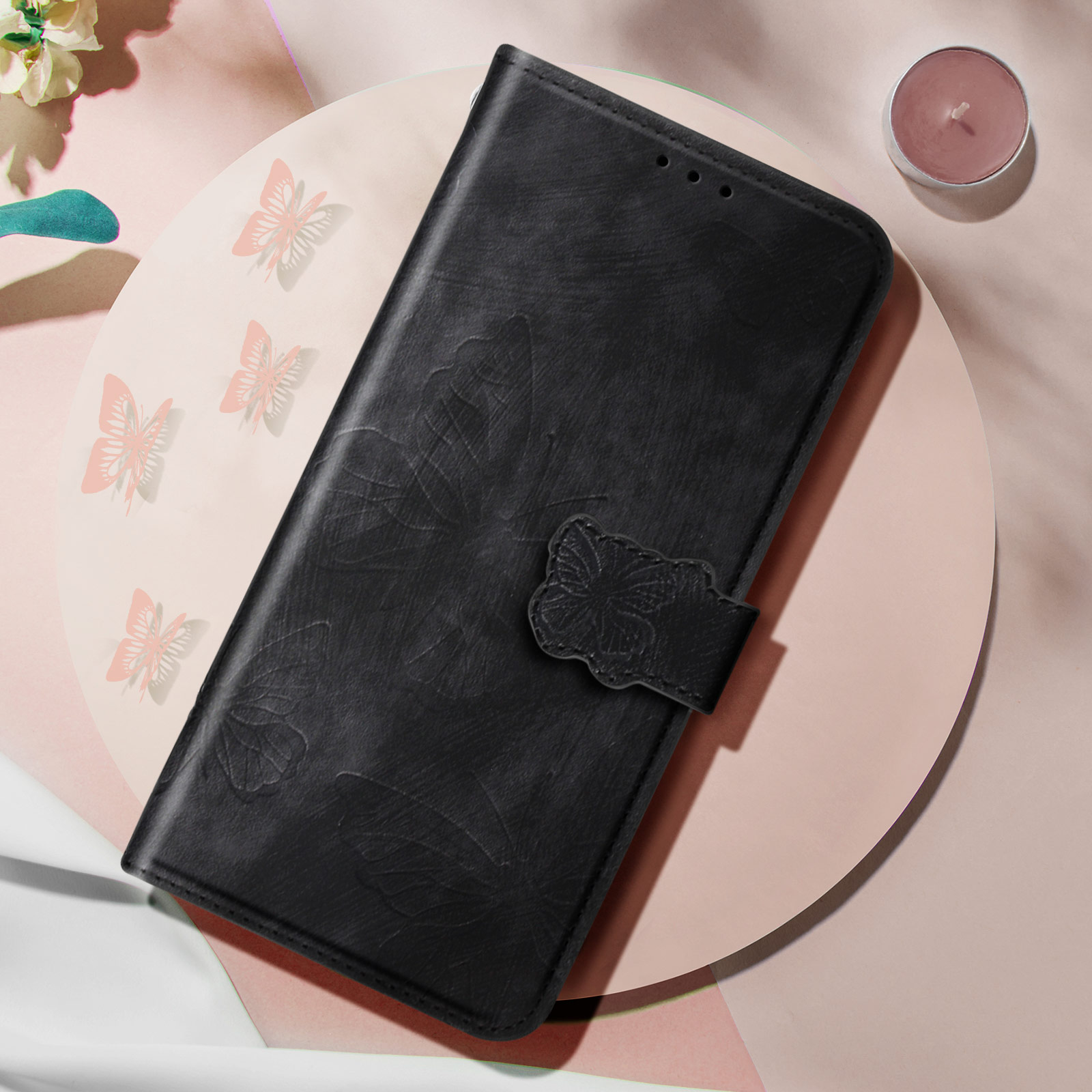 Un étui de téléphone en cuir noir avec un motif de papillon et une bougie sur une surface rose.