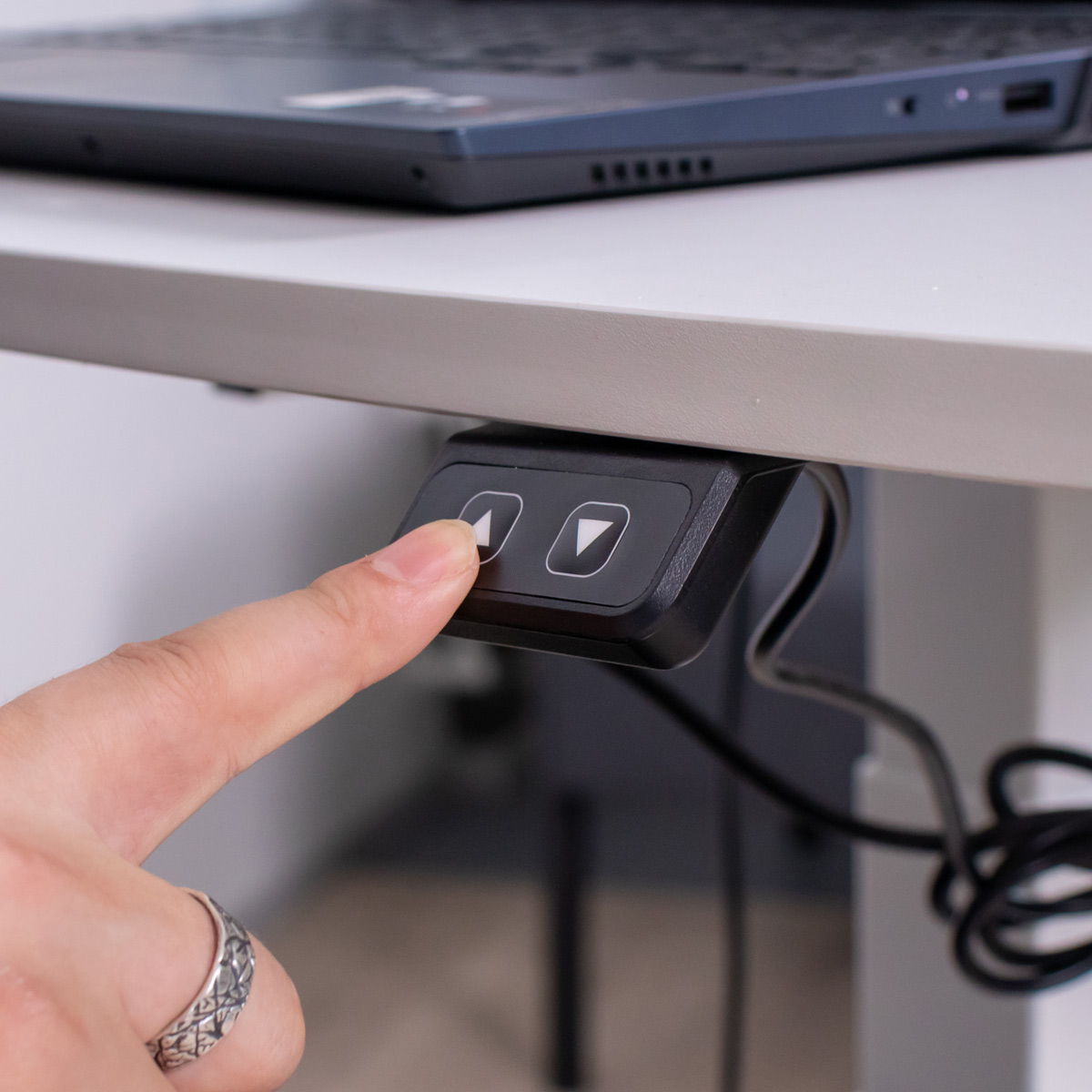 Osoba naciska przycisk strzałki w dół na czarnym panelu sterowania biurkiem.