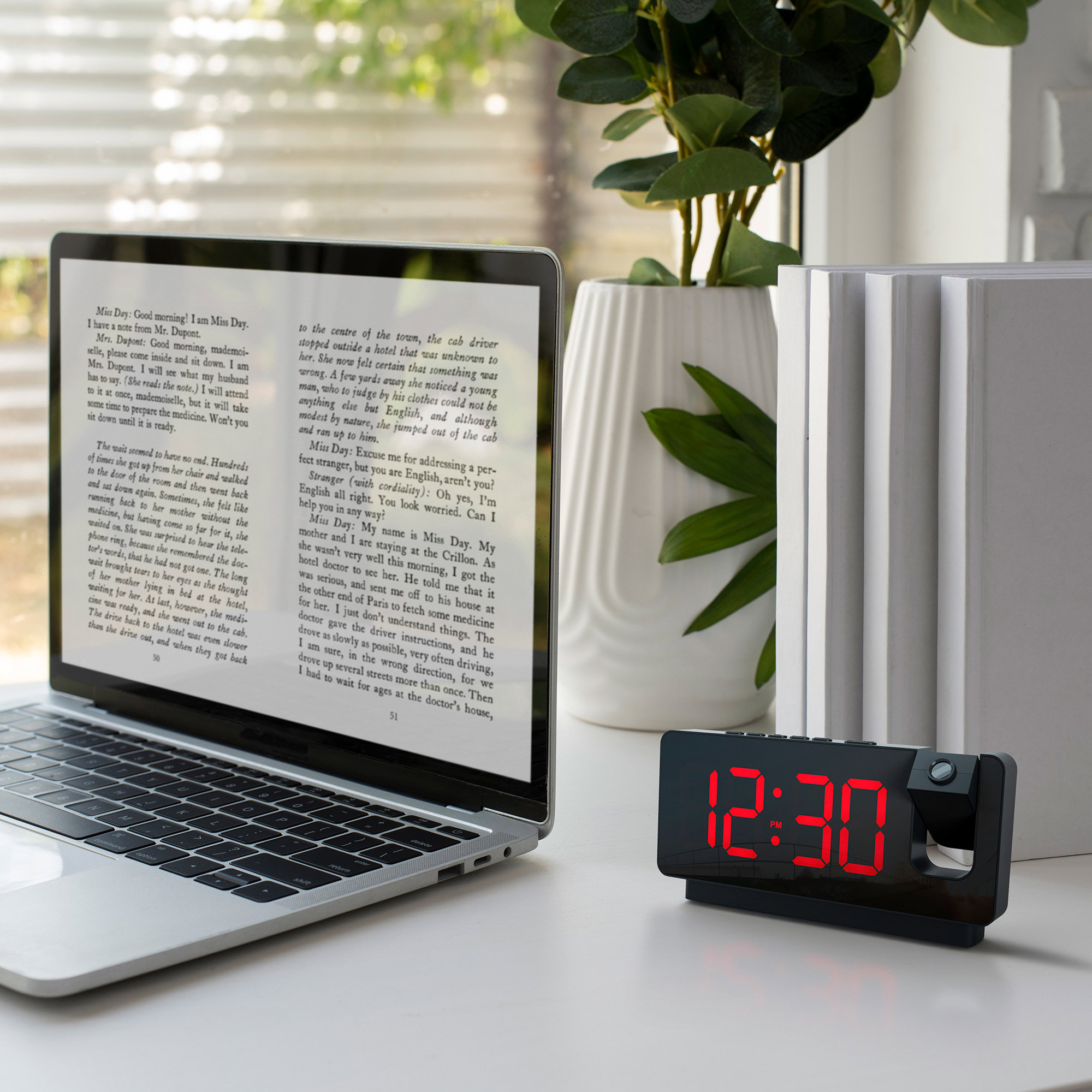 Laptop with book and digital alarm clock. The clock is red and projects time.