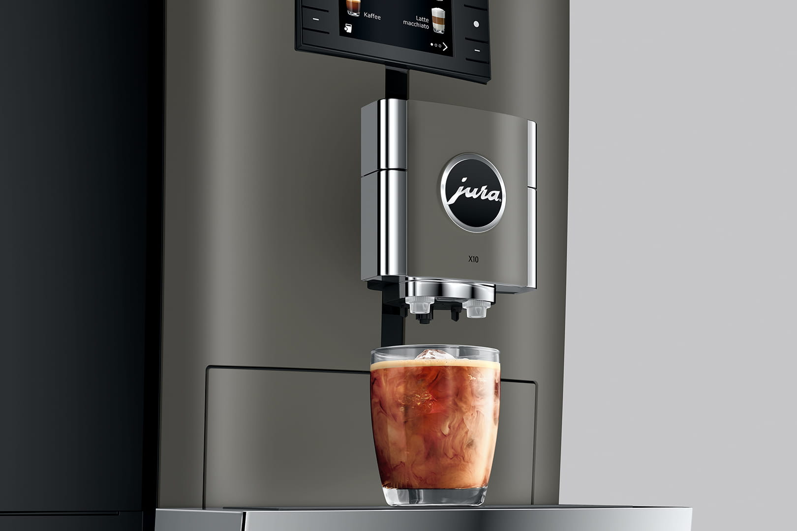 Eine Kaffeemaschine mit einem Glas Eiskaffee im Vordergrund auf grauem Hintergrund.