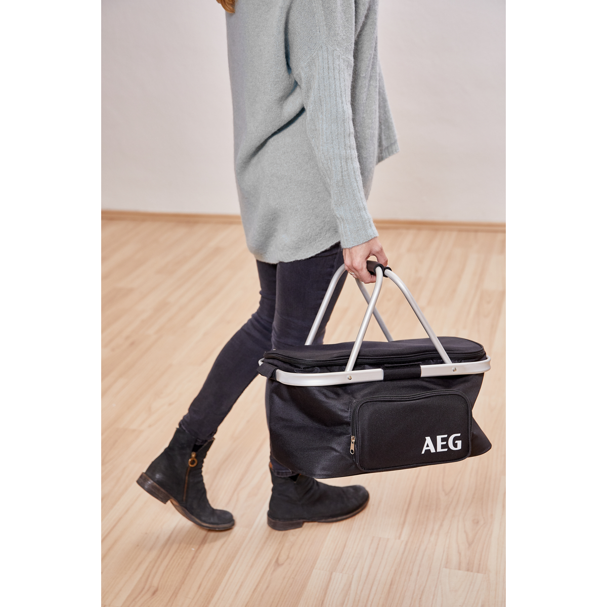 Person geht mit einer schwarzen AEG-Kühltasche auf Holzboden.