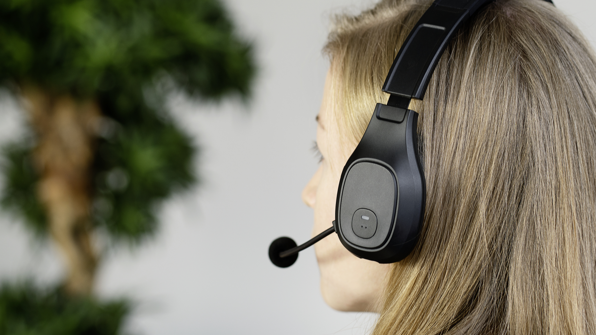 Eine blonde Frau mit einem schwarzen Headset mit Mikrofon. Der Hintergrund ist unscharf.