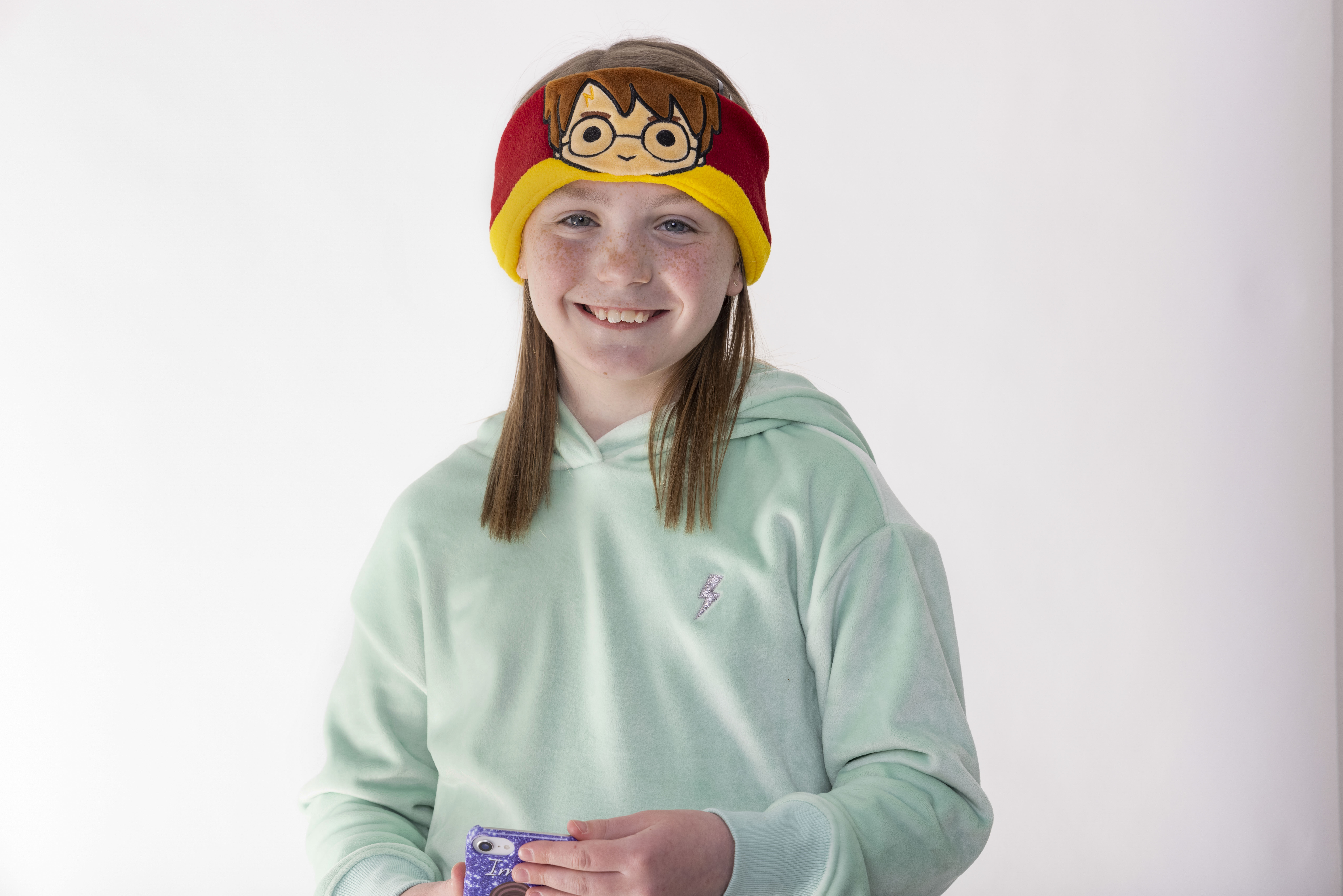 Mädchen mit Harry-Potter-Stirnband, lächelt. Sie trägt einen hellgrünen Kapuzenpullover. Weißer Hintergrund.
