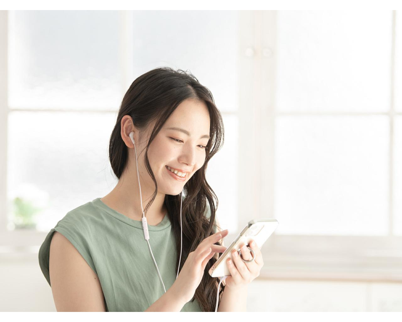 Kobieta używająca telefonu z białymi słuchawkami, uśmiechająca się w pomieszczeniu.