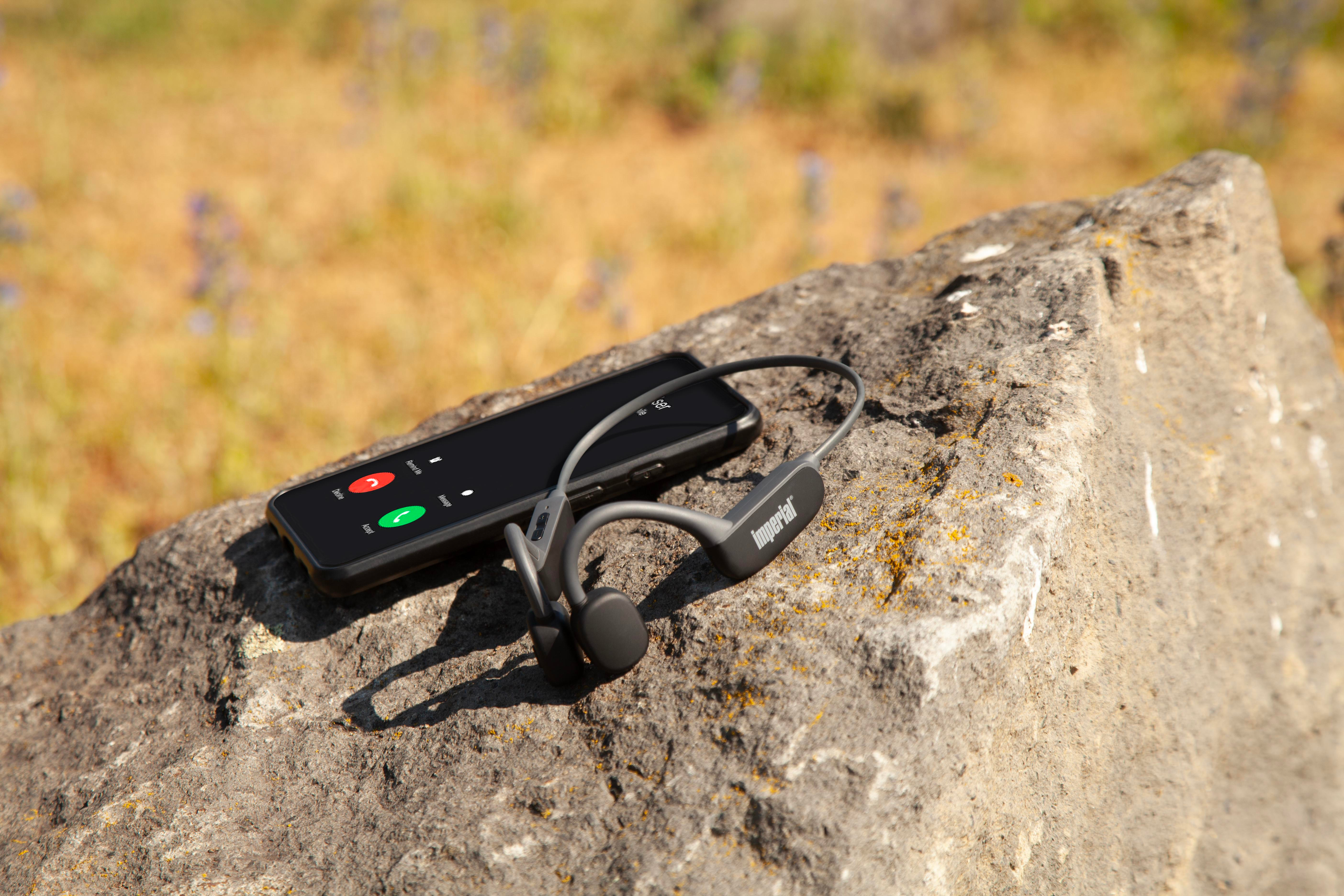 Smartfon i szare słuchawki kostne na skale, z rozmytym tłem.