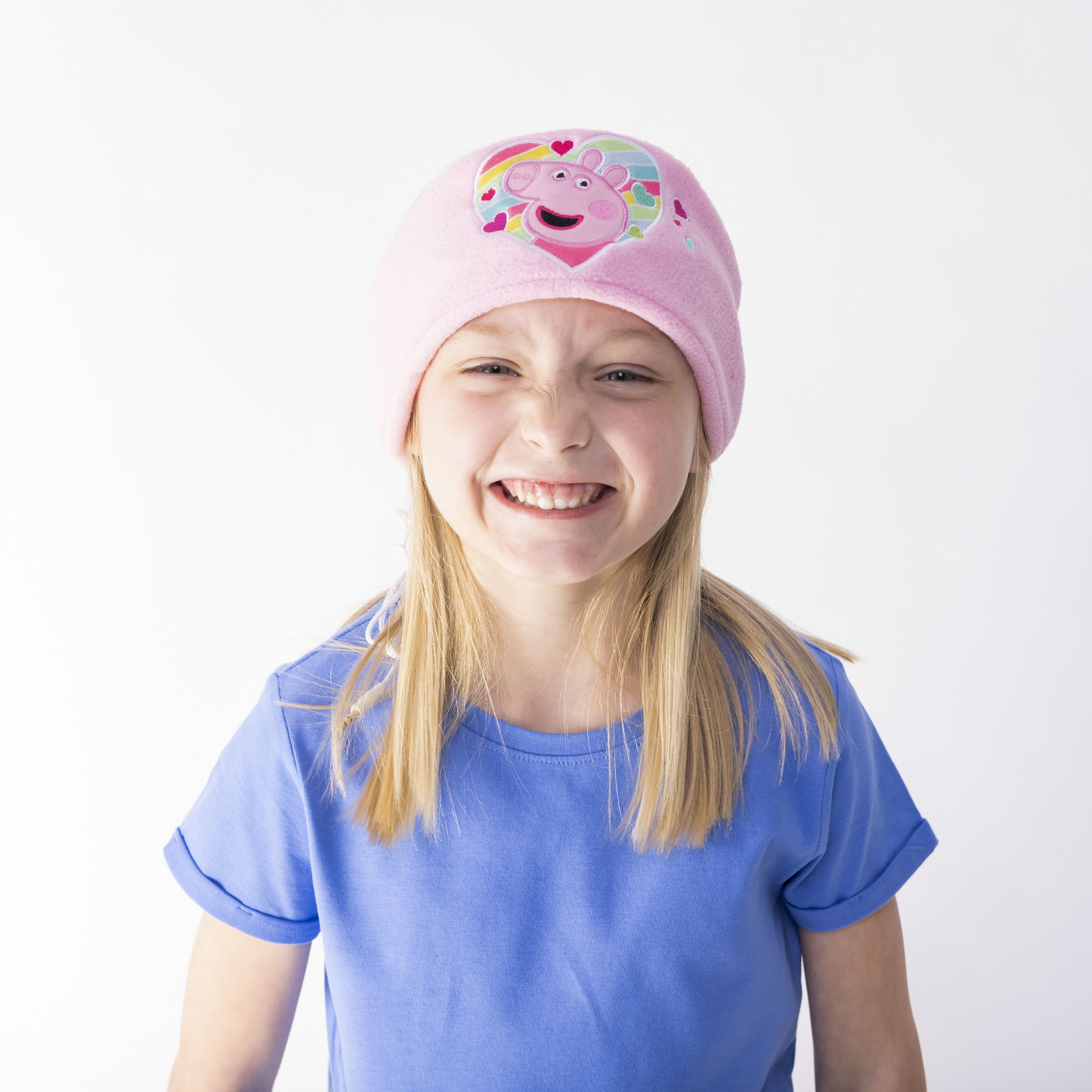 Ein lächelndes Mädchen trägt einen pinken Hut mit einem Peppa Wutz-Design.