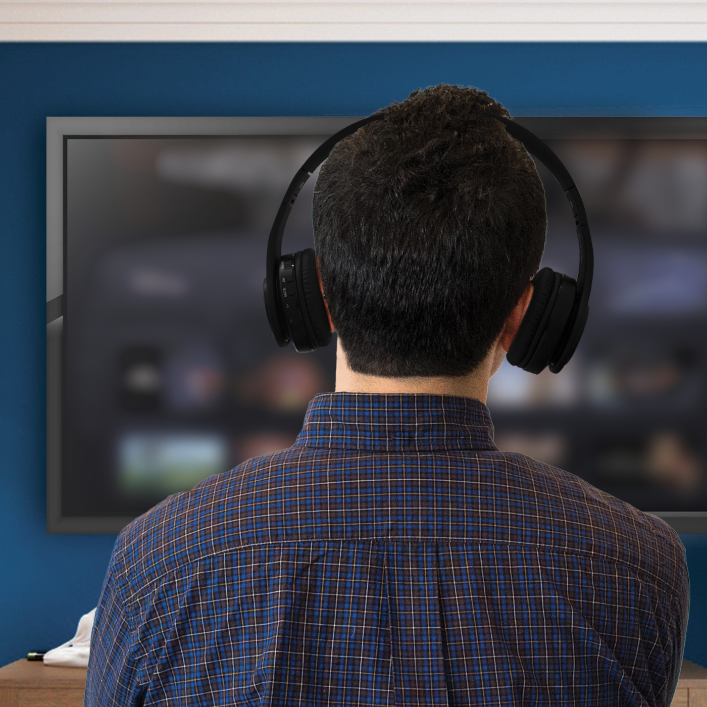 Osoba z tyłu w czarnych słuchawkach, patrząca na ekran telewizora. Niebieska ściana z tyłu.