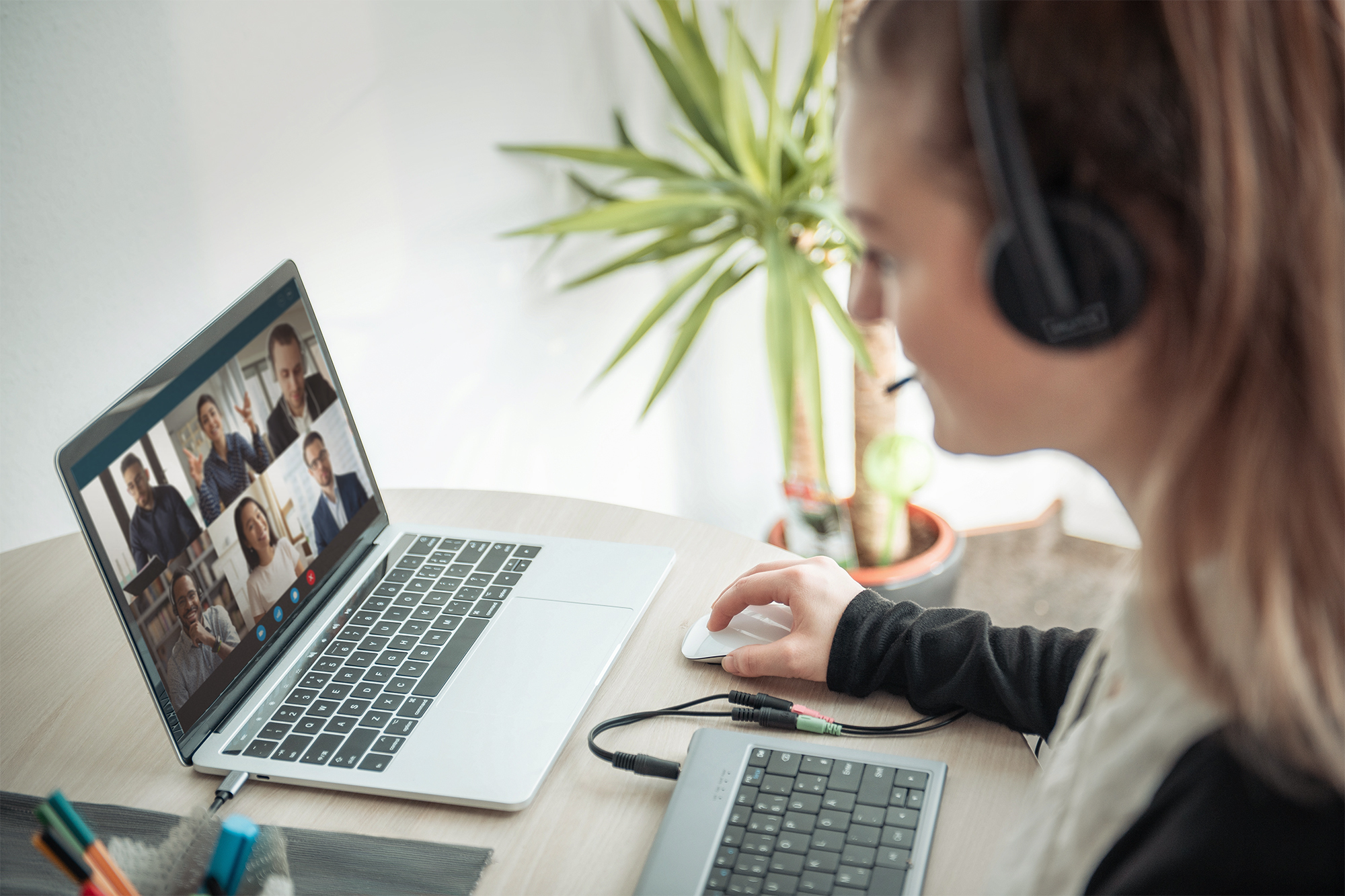 Kobieta podczas rozmowy wideo na laptopie. Używa myszy i zestawu słuchawkowego z mikrofonem.