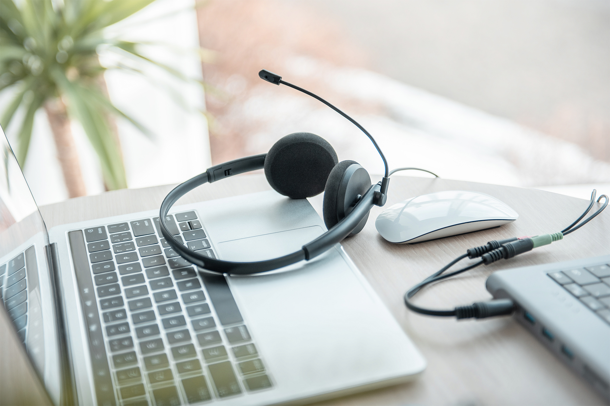 Zestaw słuchawkowy z mikrofonem, mysz i laptop na drewnianym biurku.