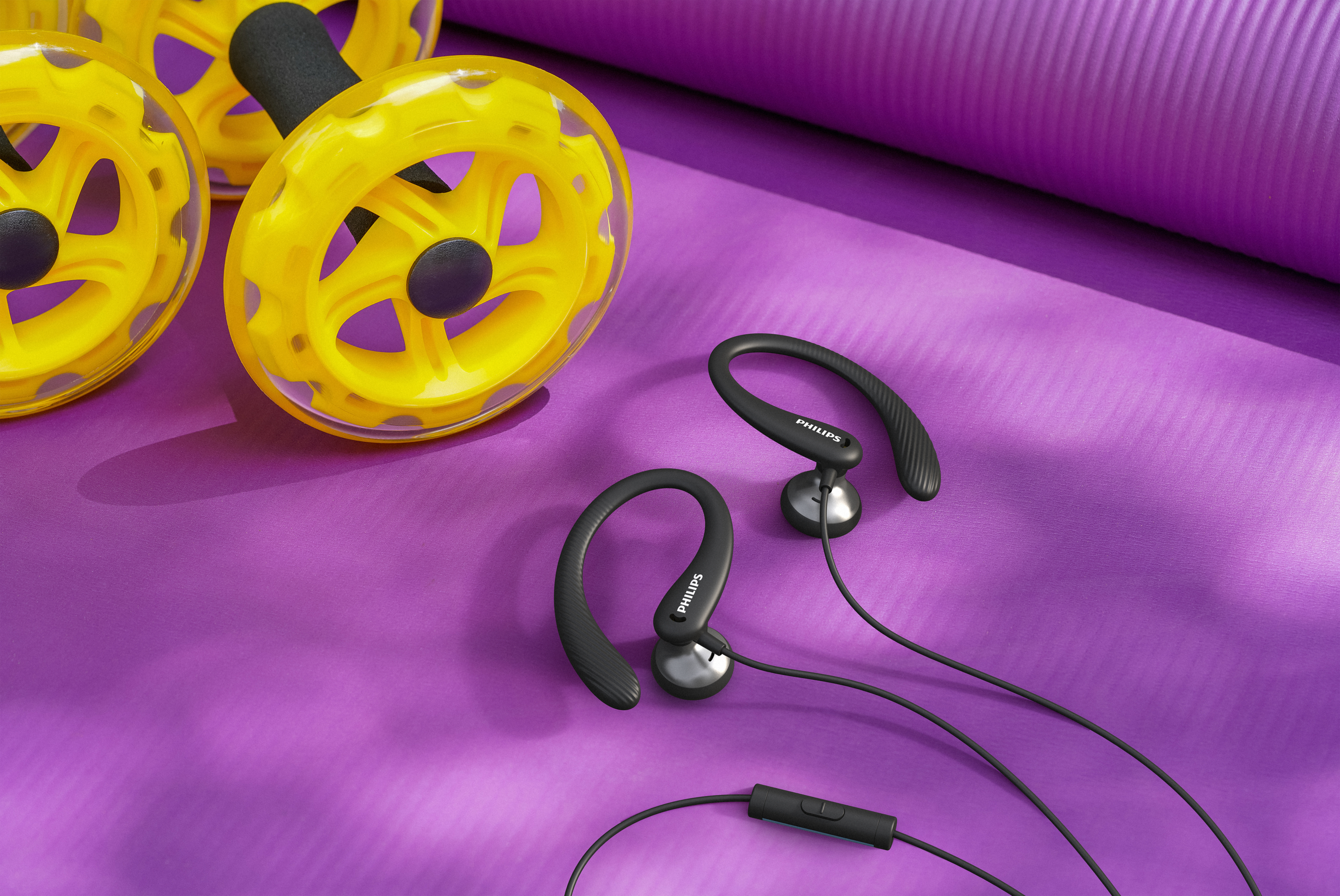 Żółte koła do ćwiczeń i czarne słuchawki na fioletowej macie.