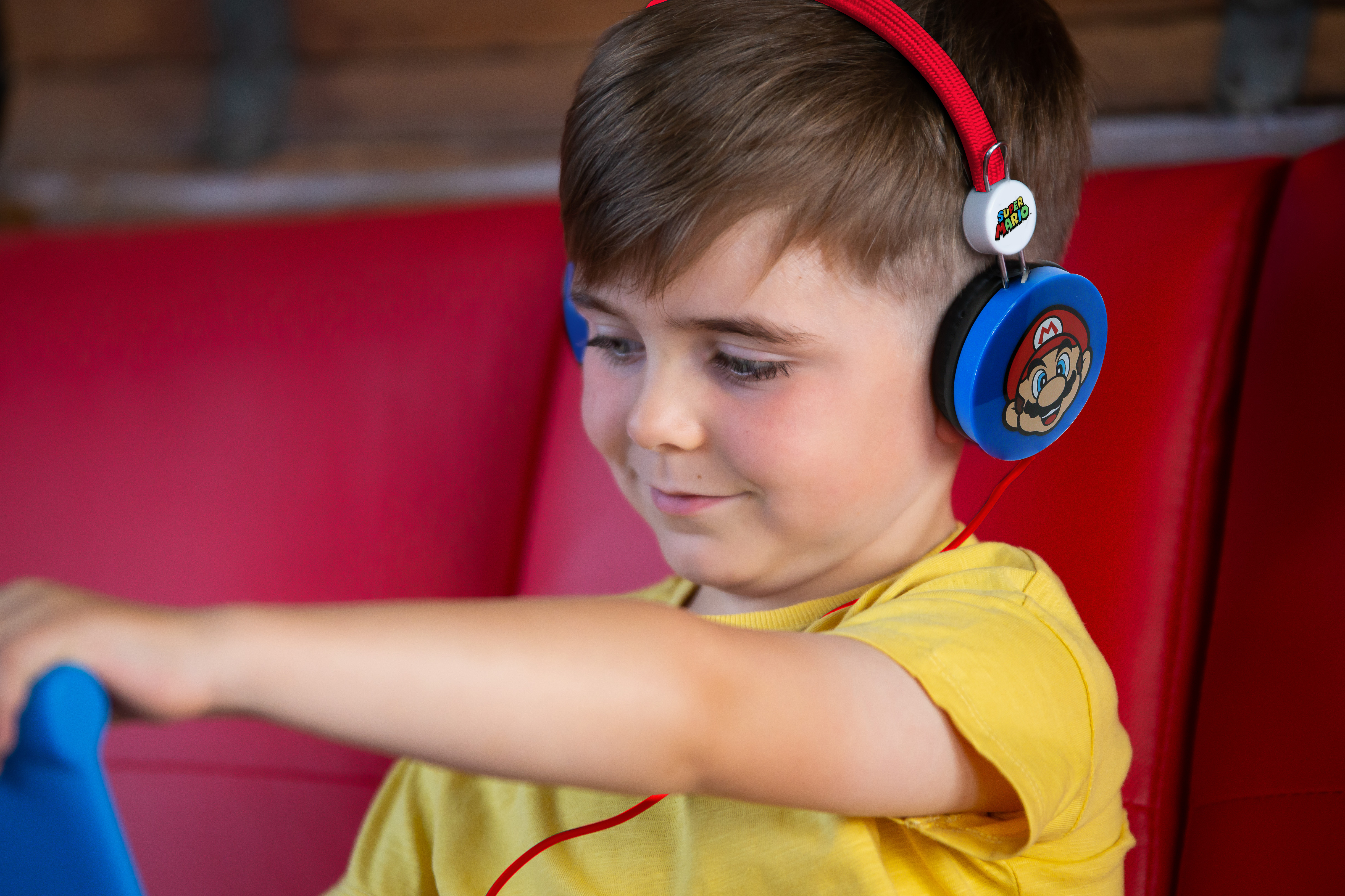 Mały chłopiec w słuchawkach Mario, uśmiechnięty, korzysta z tabletu.