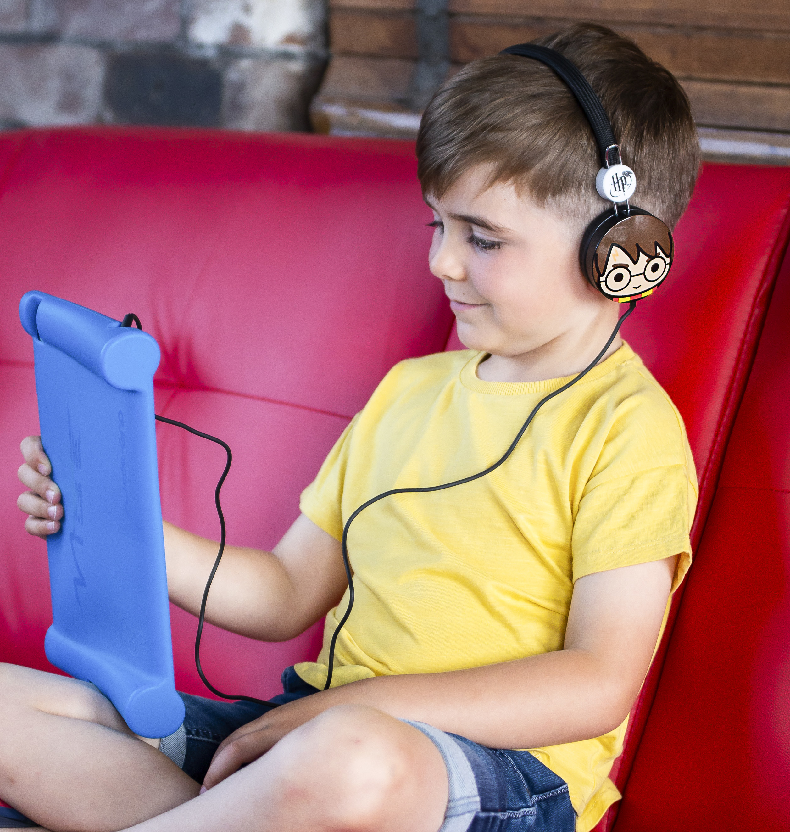 Un niño con auriculares de Harry Potter, sosteniendo una tableta azul, en un sofá rojo.